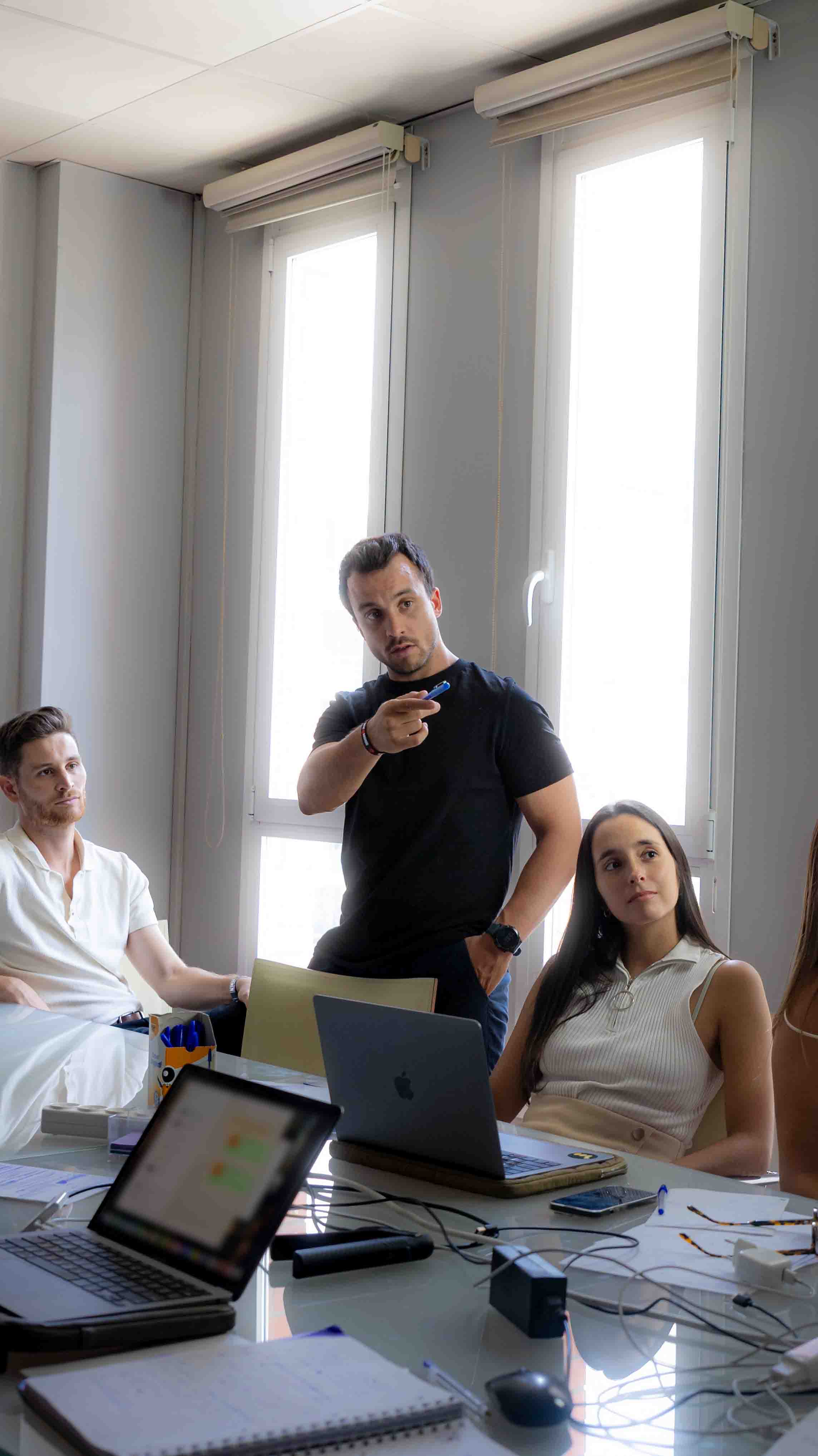 A smiling woman with her arms crossed, standing against a dark green background. She has long, dark hair.