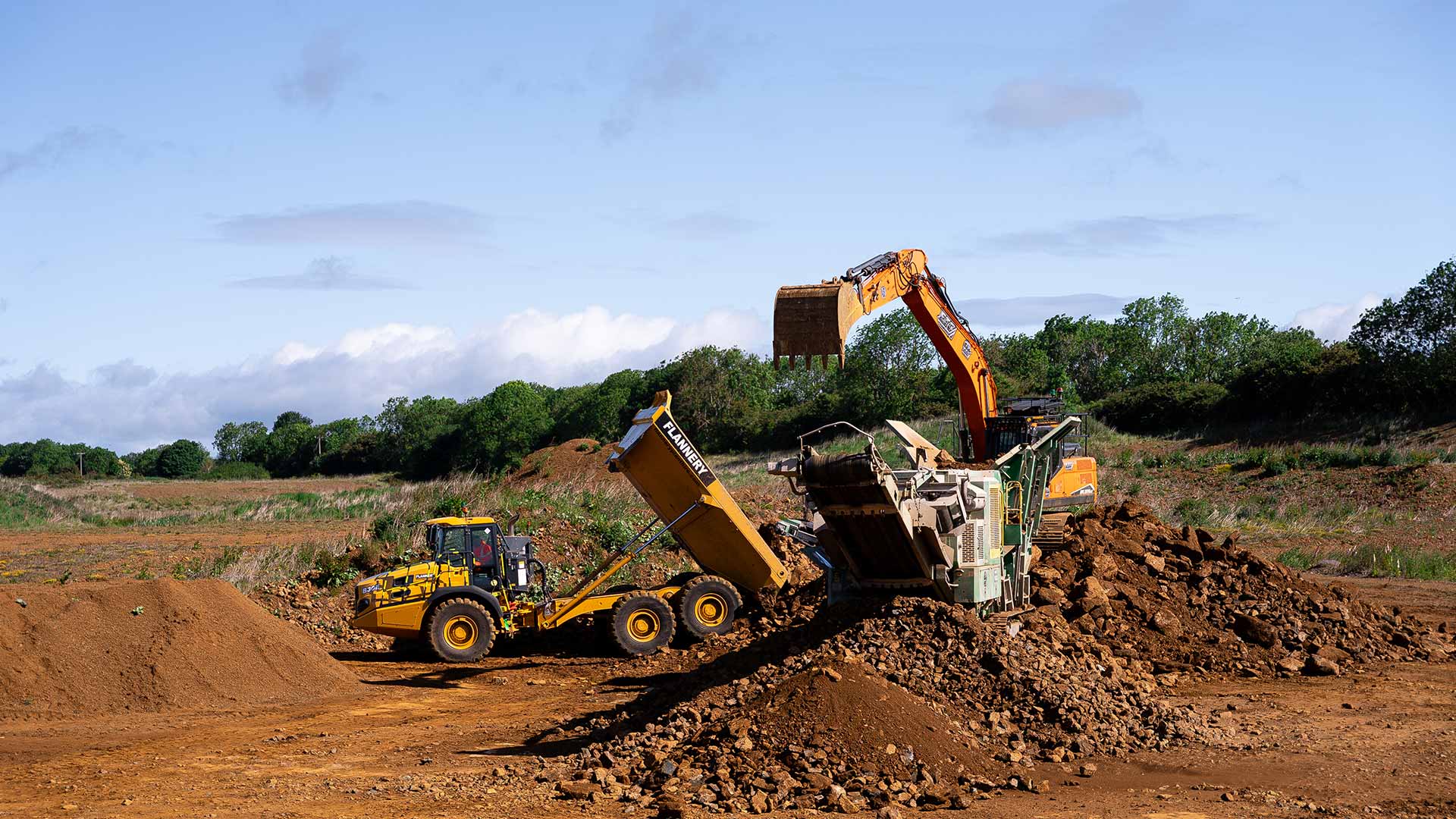 ETC excavator loading soil into McCloskey screener while Flannery dumper offloads material on UK earthworks site
