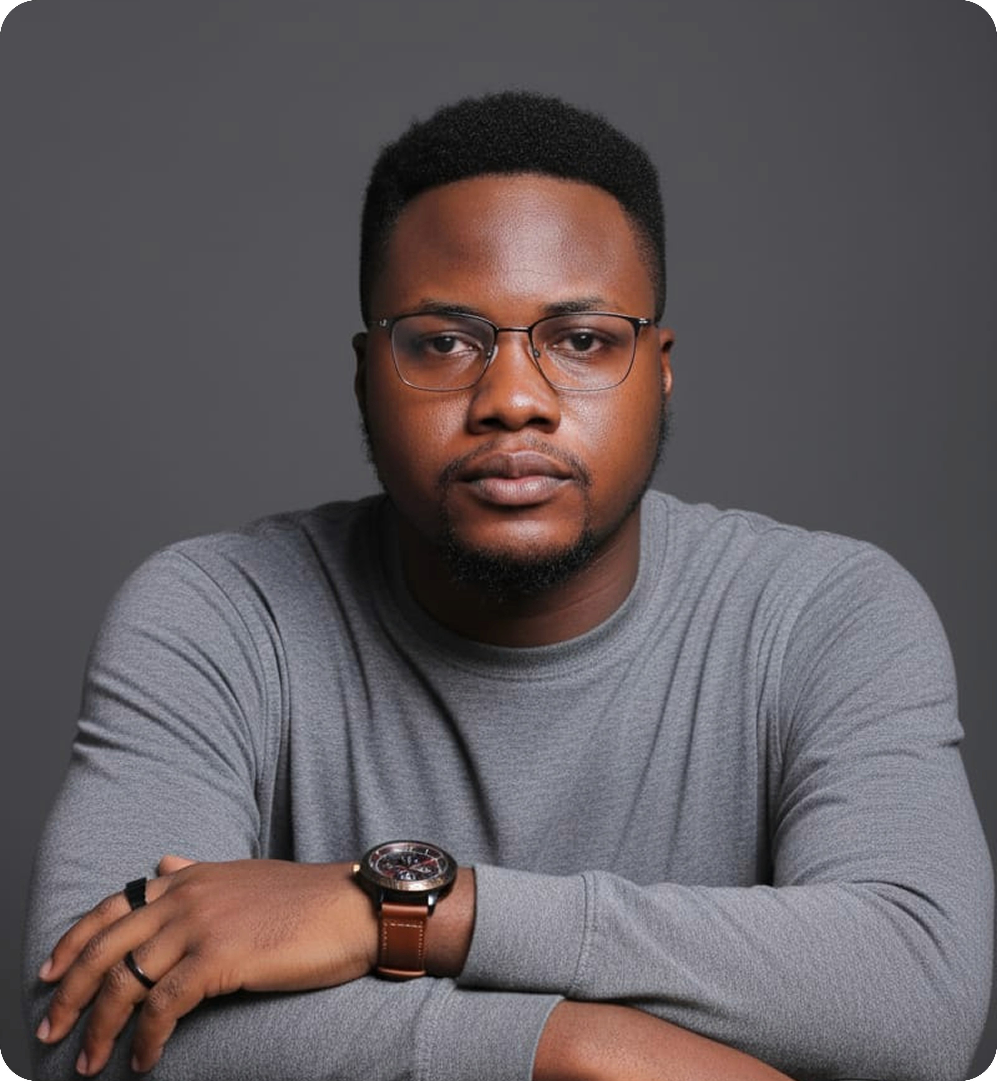 Dark male, has a calm, confident expression and is looking directly at the camera with glasses on.