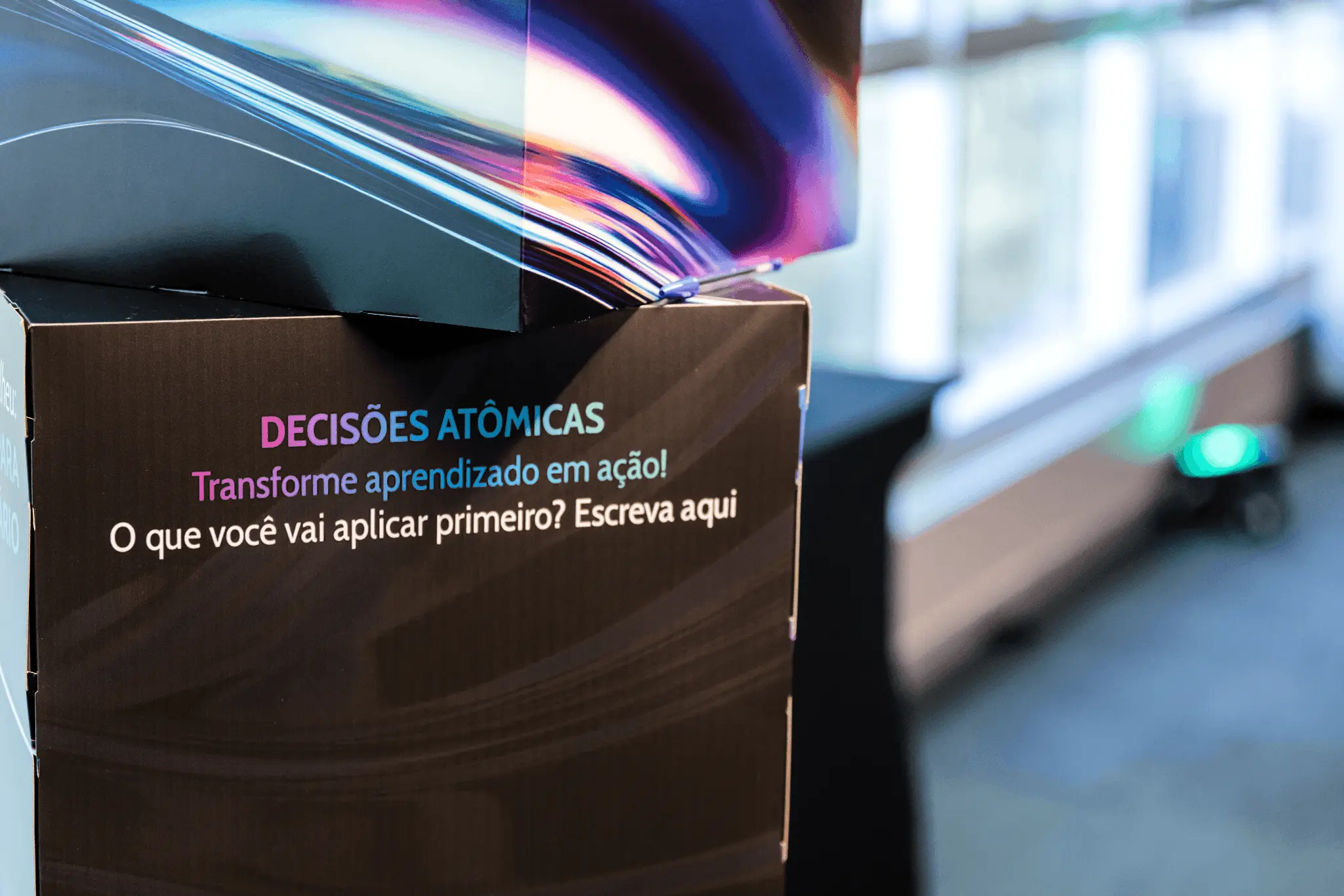 A close-up of a dark surface with a colorful light reflection above it, possibly inside a modern space. Atomic Growth Club. Atomic Group. Br24. 
