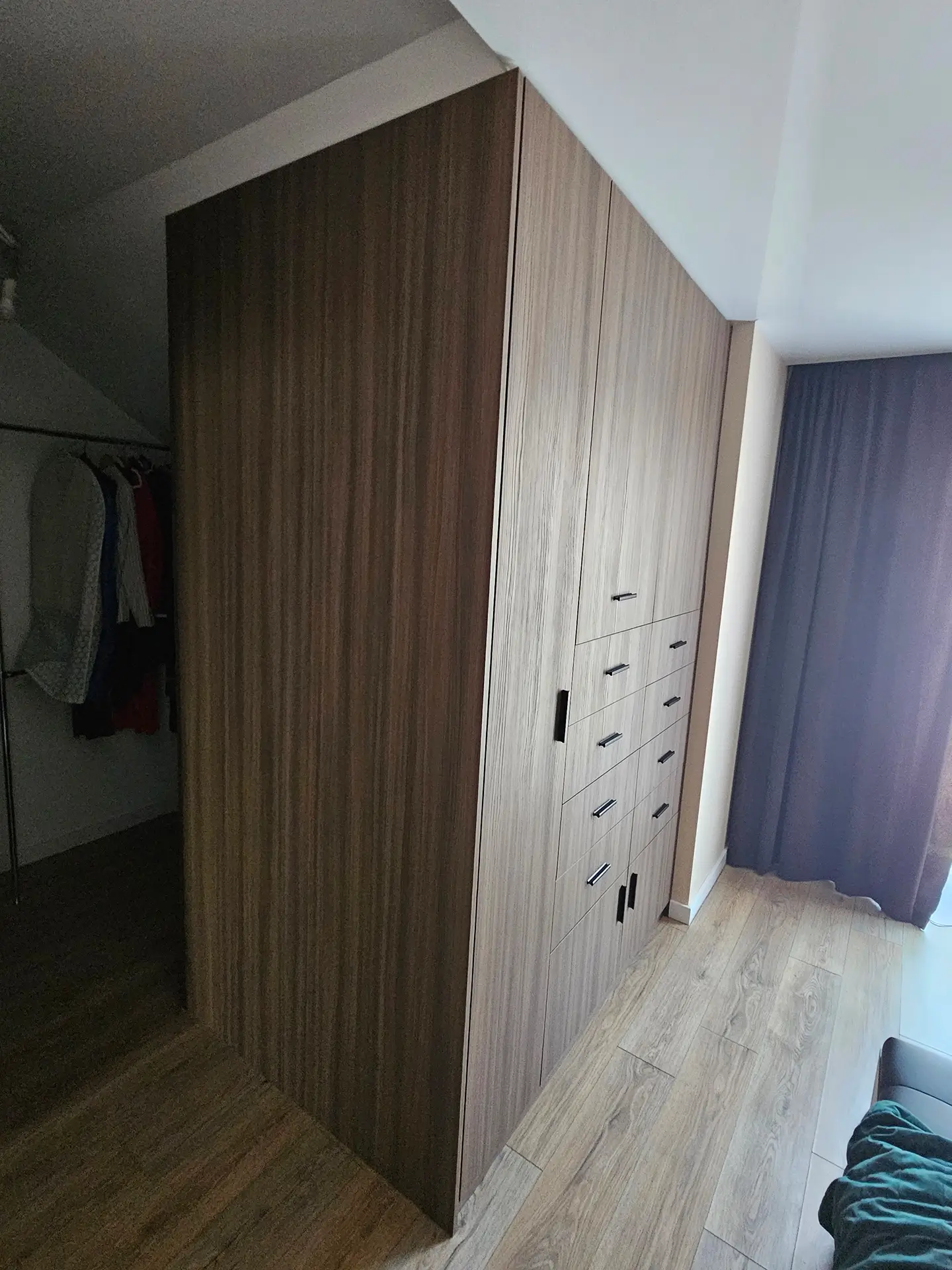 Nowoczesna szafa w sypialni ze wzorem drewna, wykonana pod skosem i dopasowana do przestrzeni.