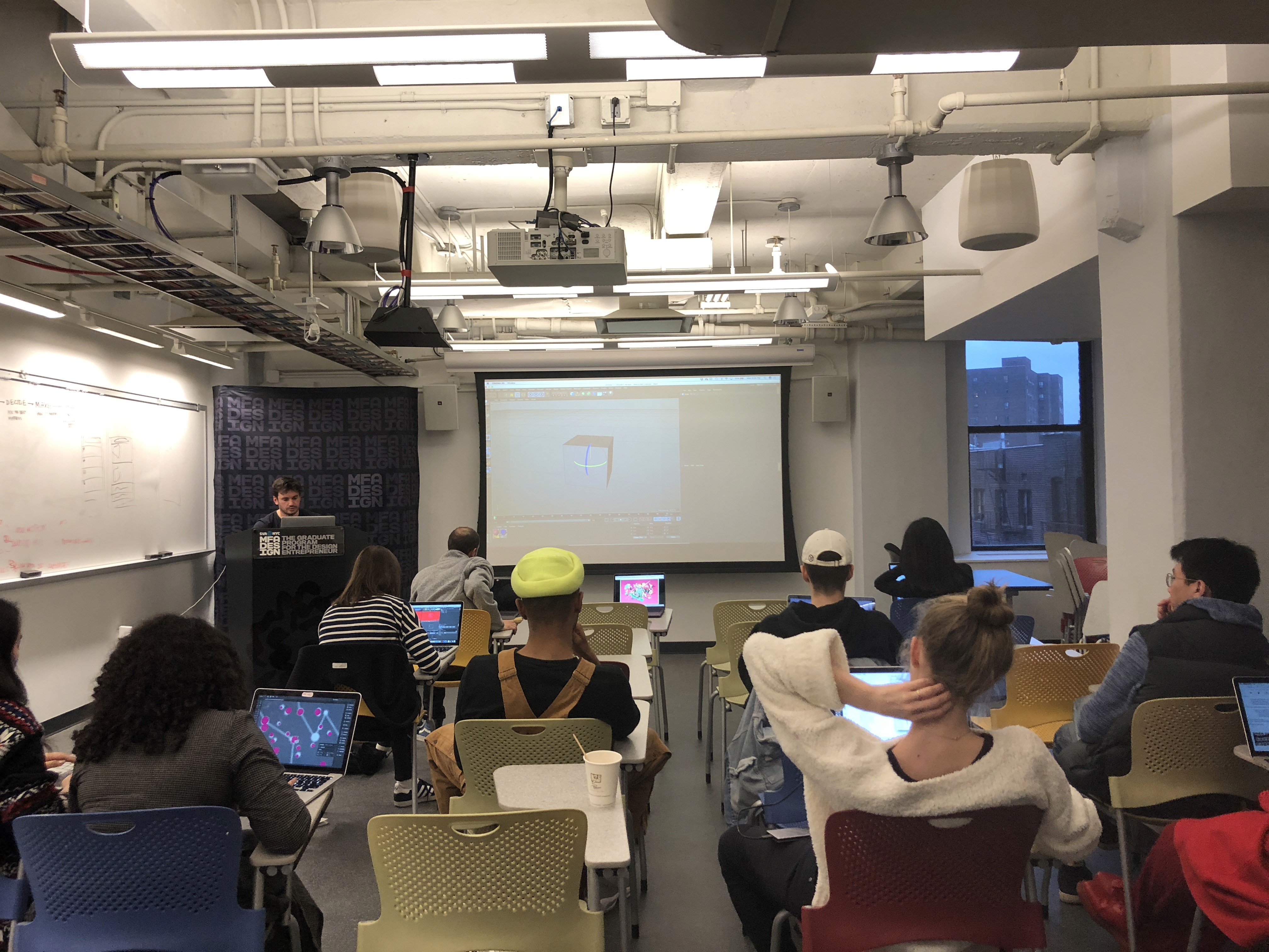 A photo from a classroom showing students sitting at their desks and following a lecture on a screen projector.