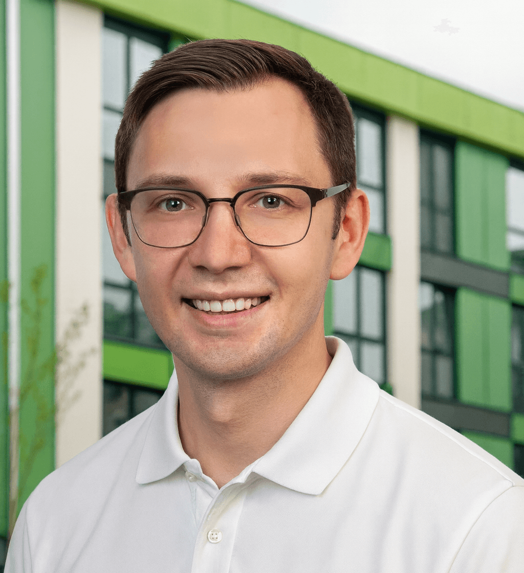 Christian Scheller, Energieberater bei wattkonzept, mit weißem Poloshirt vor modernem Gebäude mit grünen Fassadenelementen.