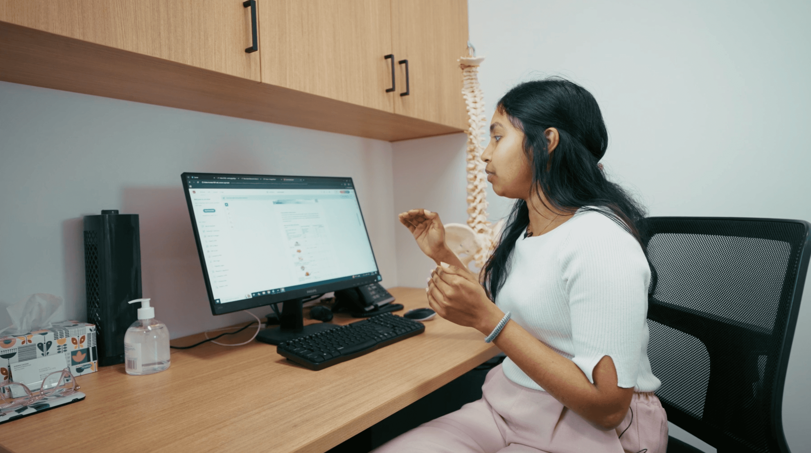 Woman seated at a desk, engaged with a computer screen during a consultation or treatment planning session in a physiotherapy clinic.