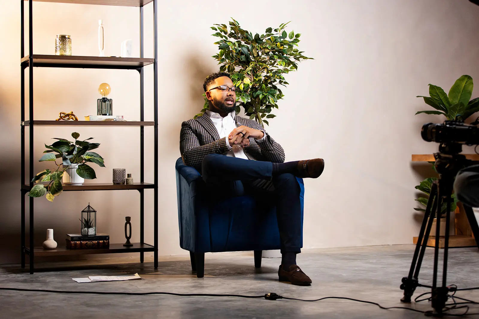 Chris Lewis sits confidently in a modern chair, smiling and dressed in a checkered blazer and white shirt. The warm wood background and relaxed pose reflect his approachable professionalism and expertise in helping clients navigate the home loan process.