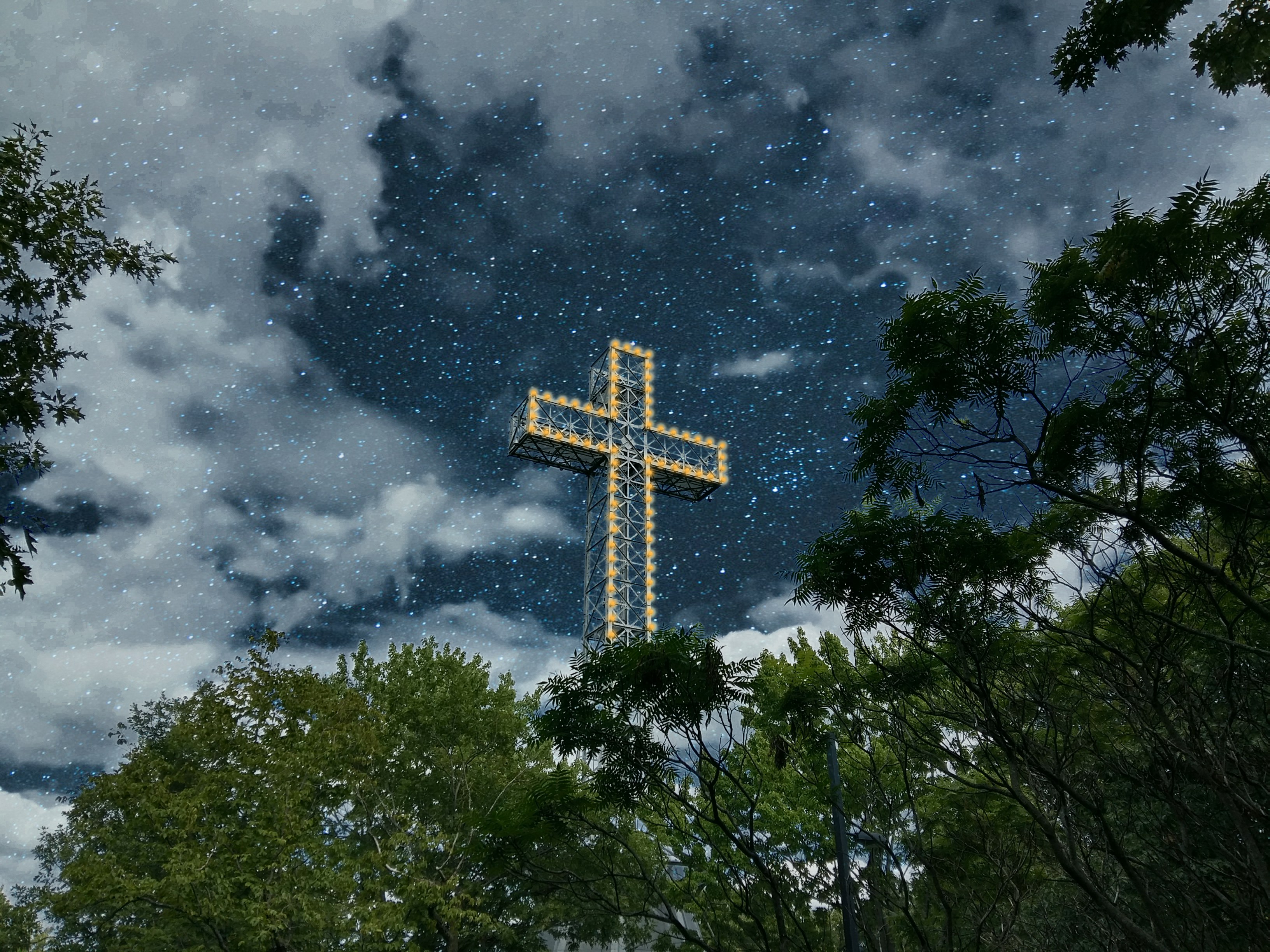brown cross on green trees under white clouds