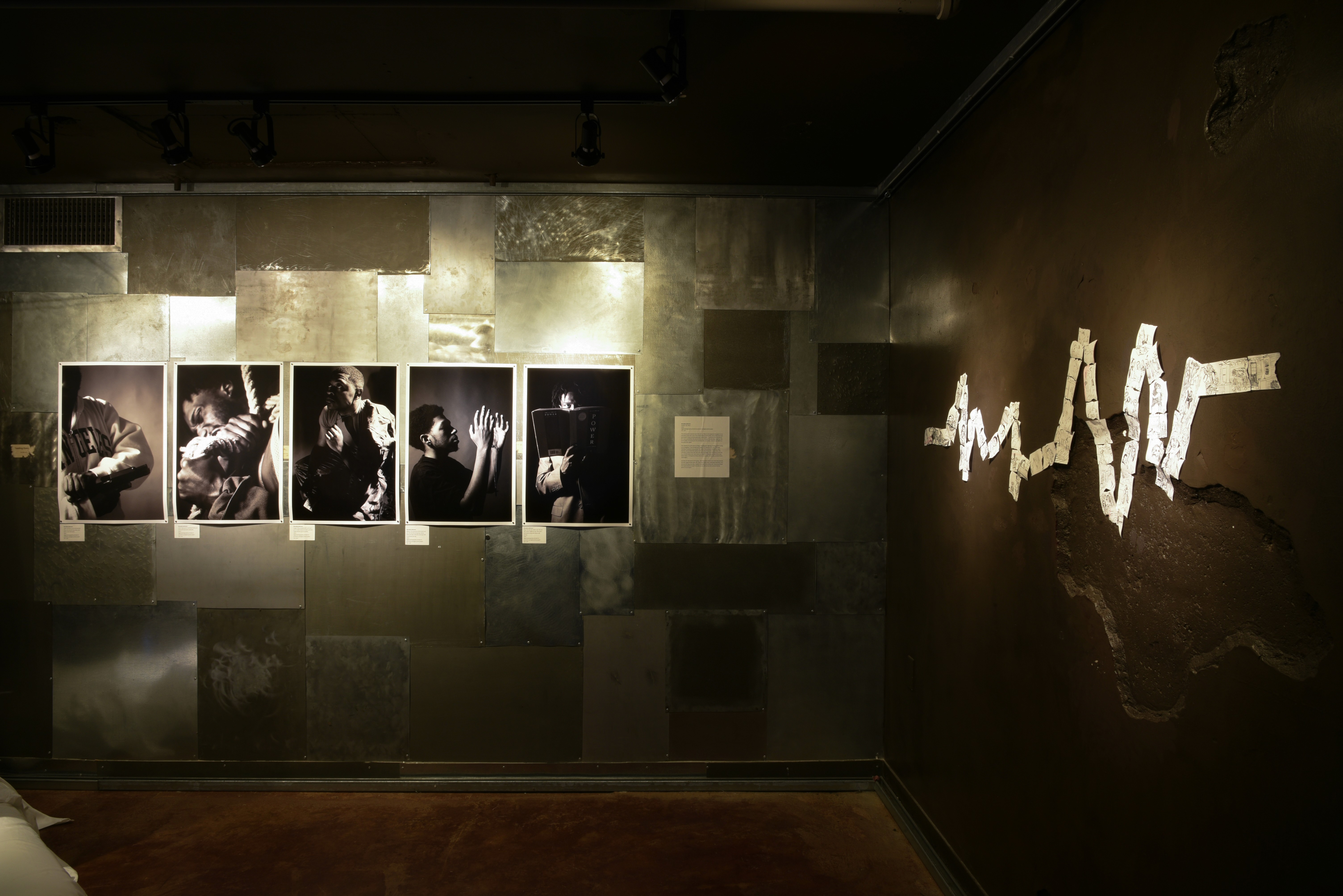 Pictures and a paper sculpture hung up on the wall of an art gallery in a dimly lit room