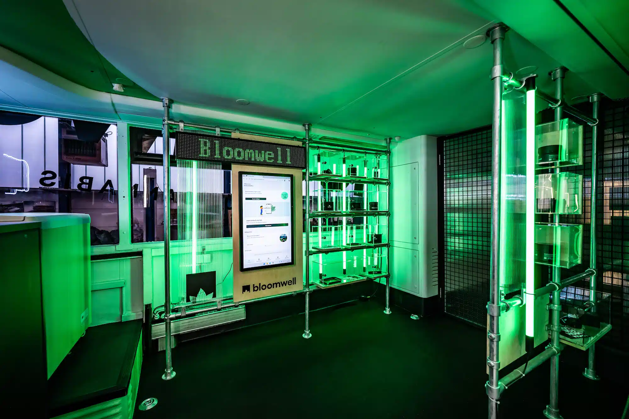 Bloomwell Cannabis App – bus interior with green neon lighting, exhibition shelves and Bloomwell branding