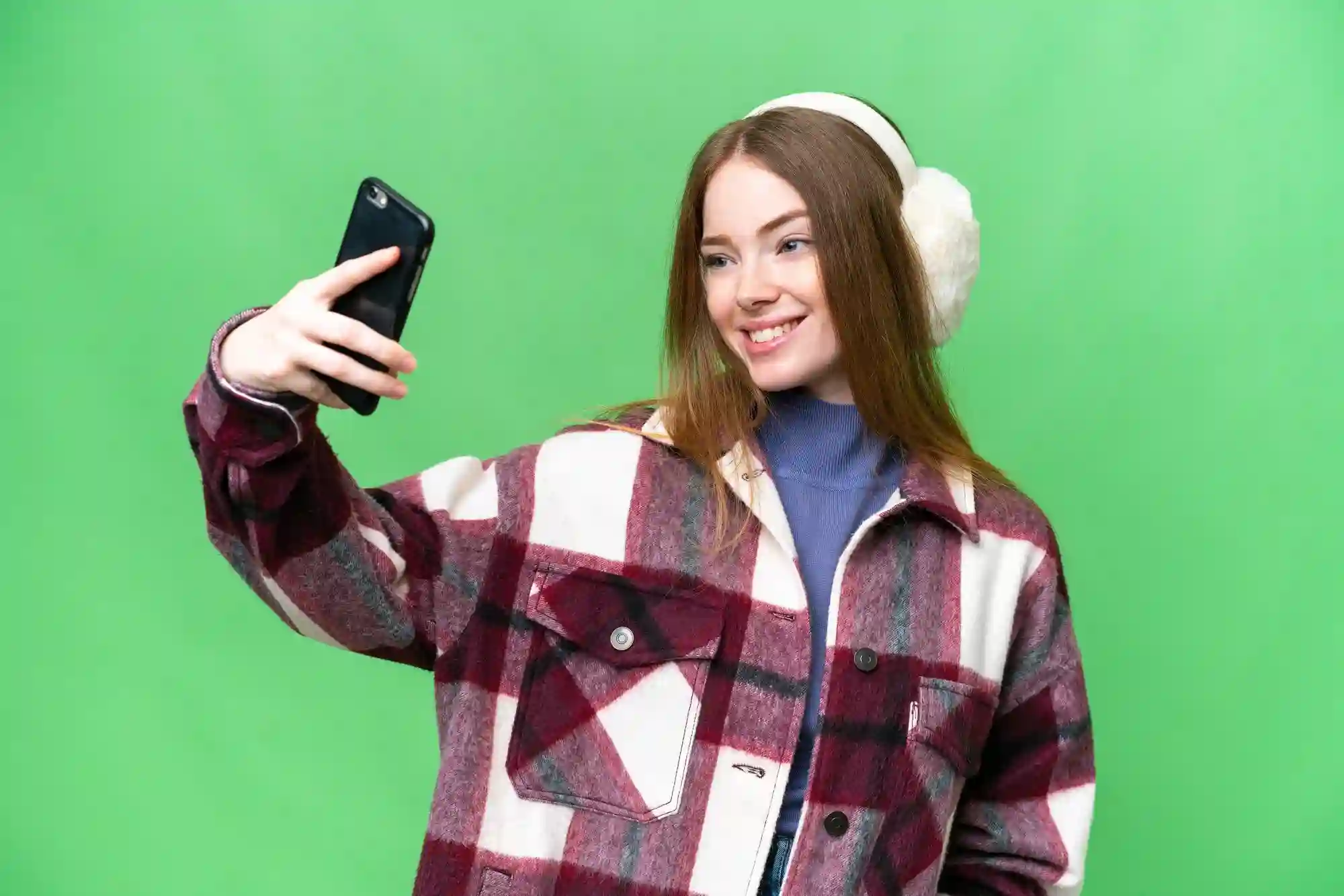 Young woman in plaid taking a selfie on green background.