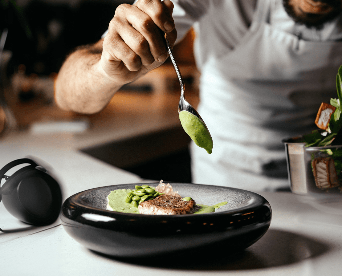 Chef garnit un plat avec une cuillère de purée verte.