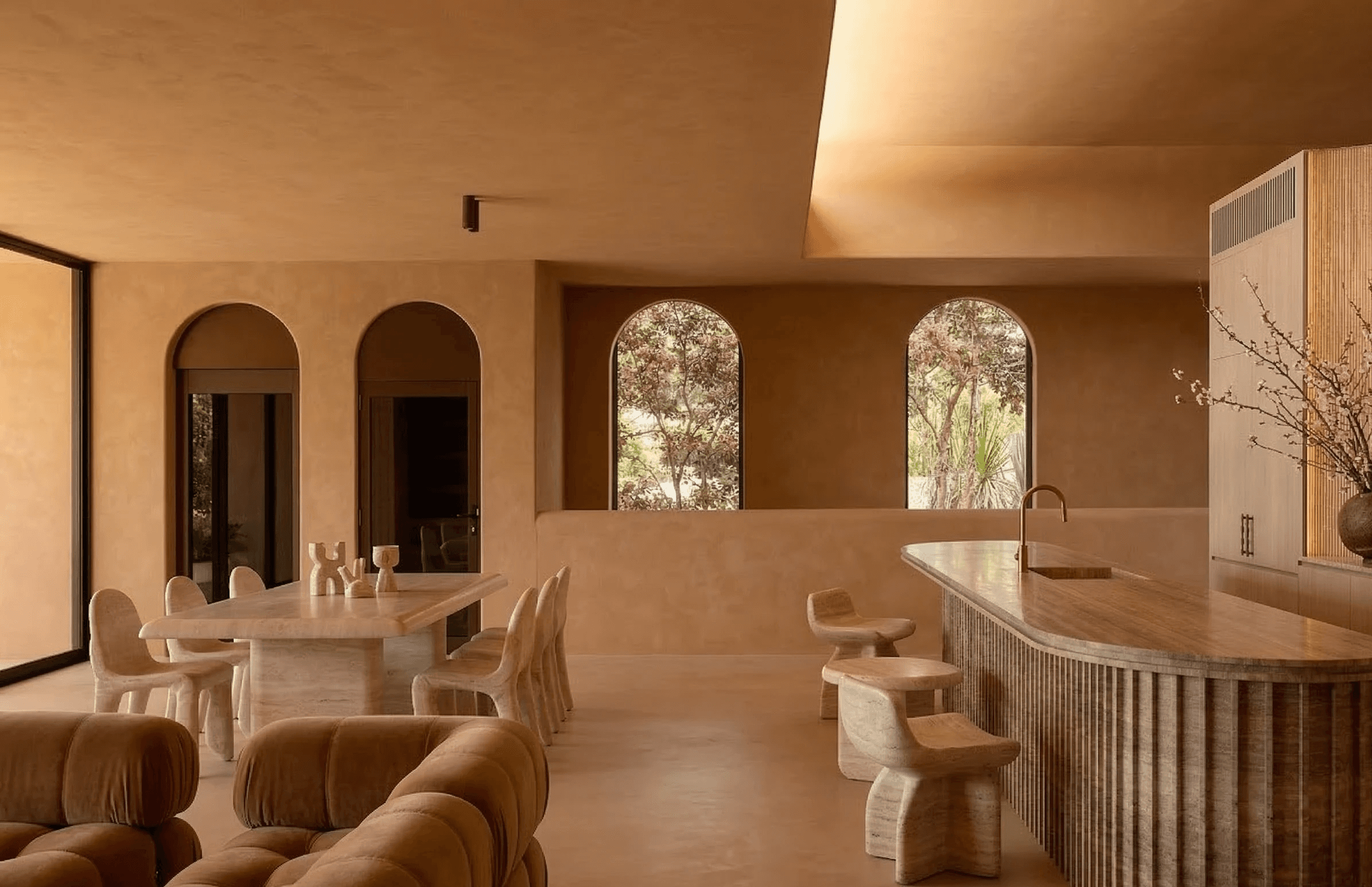 Golden hour architectural courtyard with terracotta walls, overhead beams, and planted walkways lined with trees.