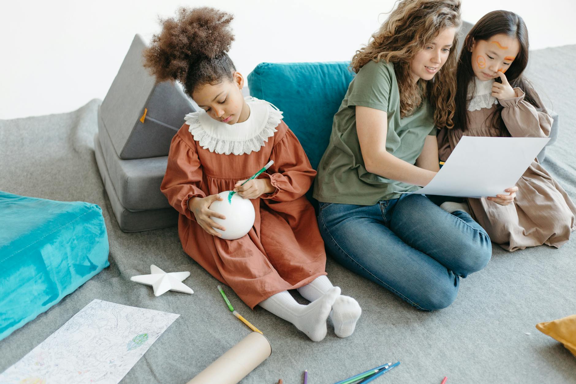 Two young students collaborate at a low wooden desk, one using a chunky crayon and the other using a thin marker.