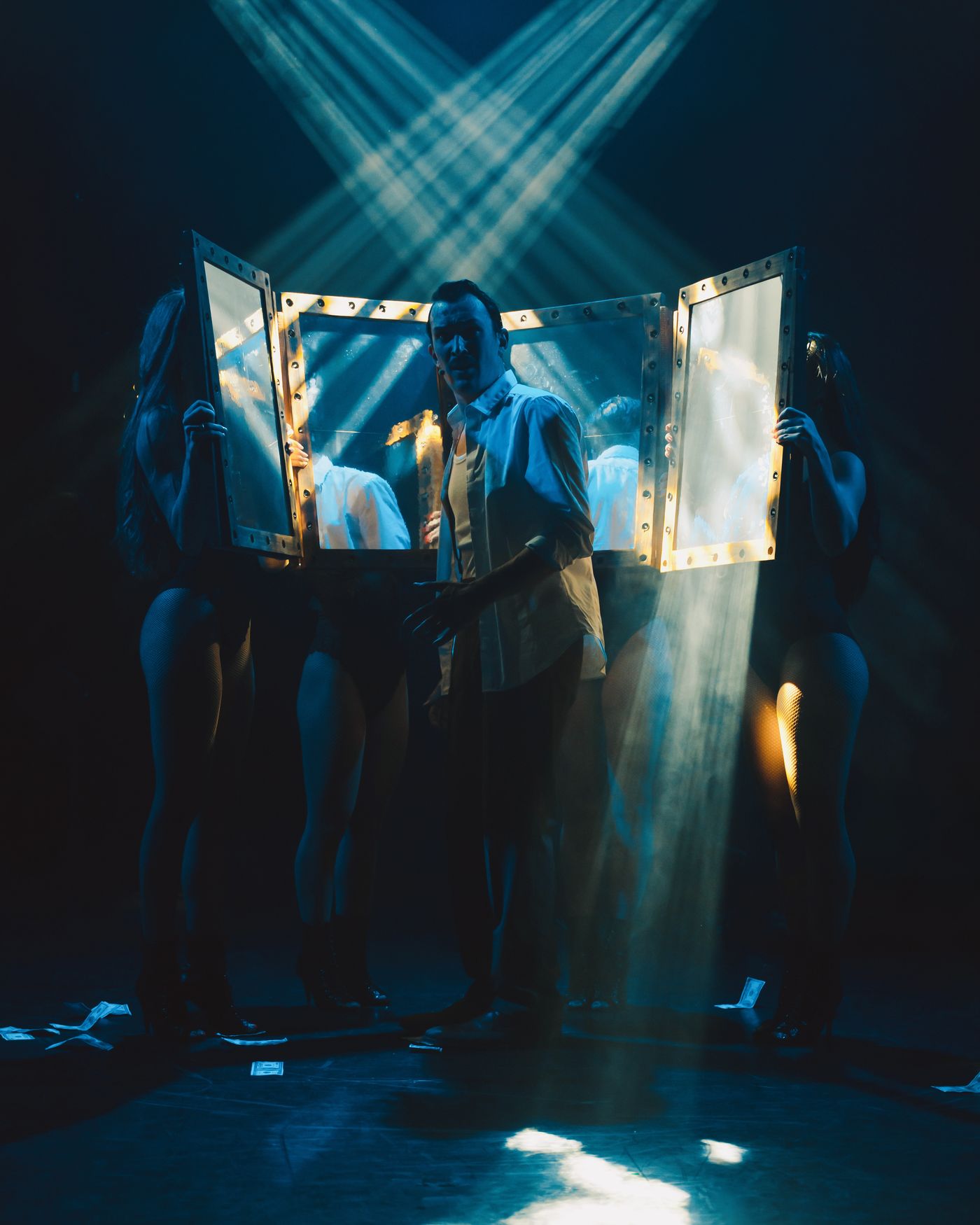 Sur scène, James Warner et ses muses entourés de miroirs, sous des faisceaux de lumière bleue qui se croisent dans la fumée