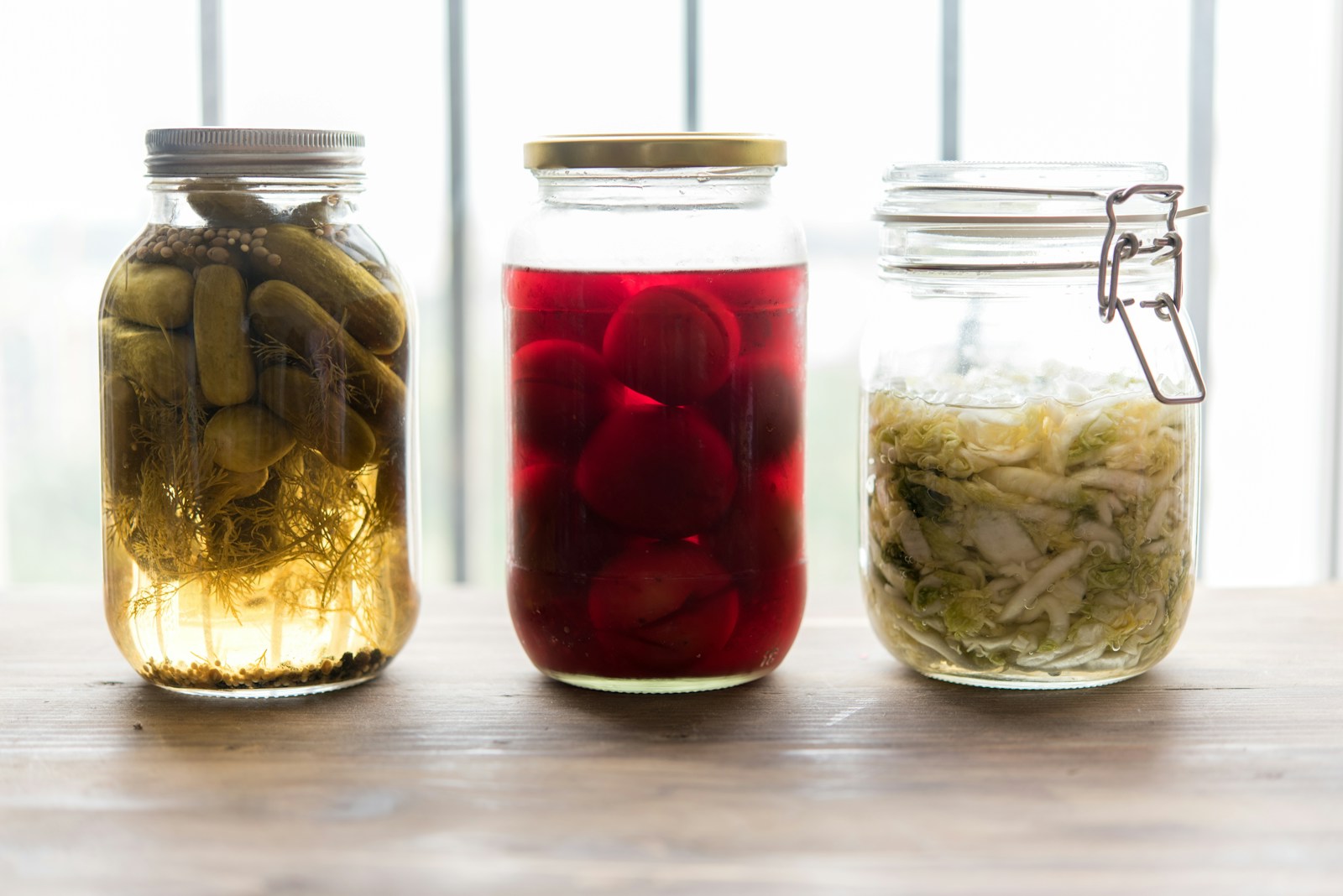 Three glass jars of fermented foods including pickles, pickled beets, and sauerkraut, foods that may help support the gut microbiome