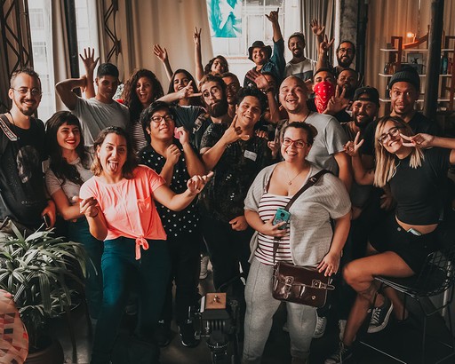 A diverse and joyful group of people posing for a photo with cheerful expressions and playful gestures, in a cozy indoor setting with warm lighting