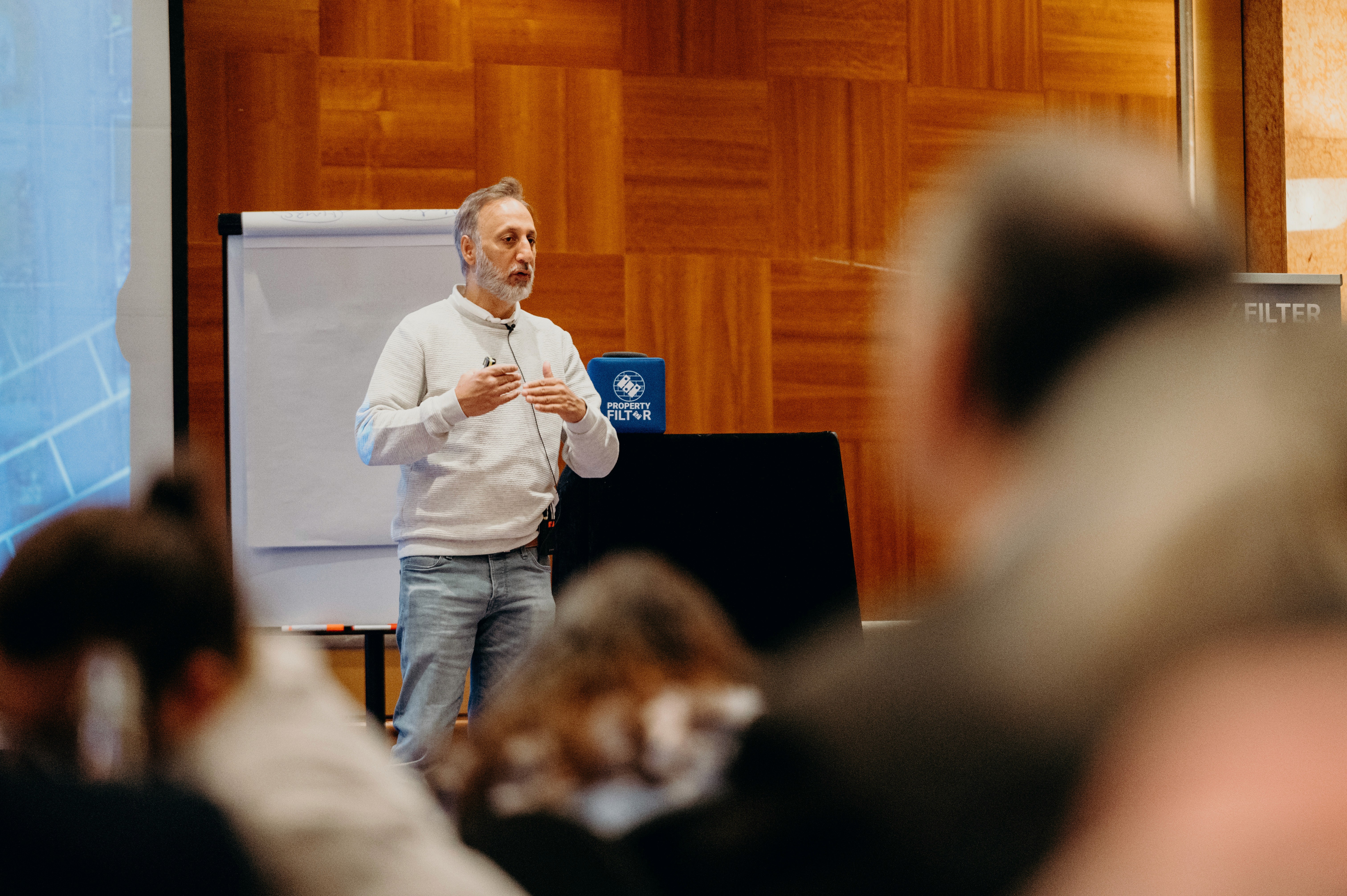Hanif Khan: Bald man with grey beard wearing light colored shirt presenting with flipchart in conference setting
