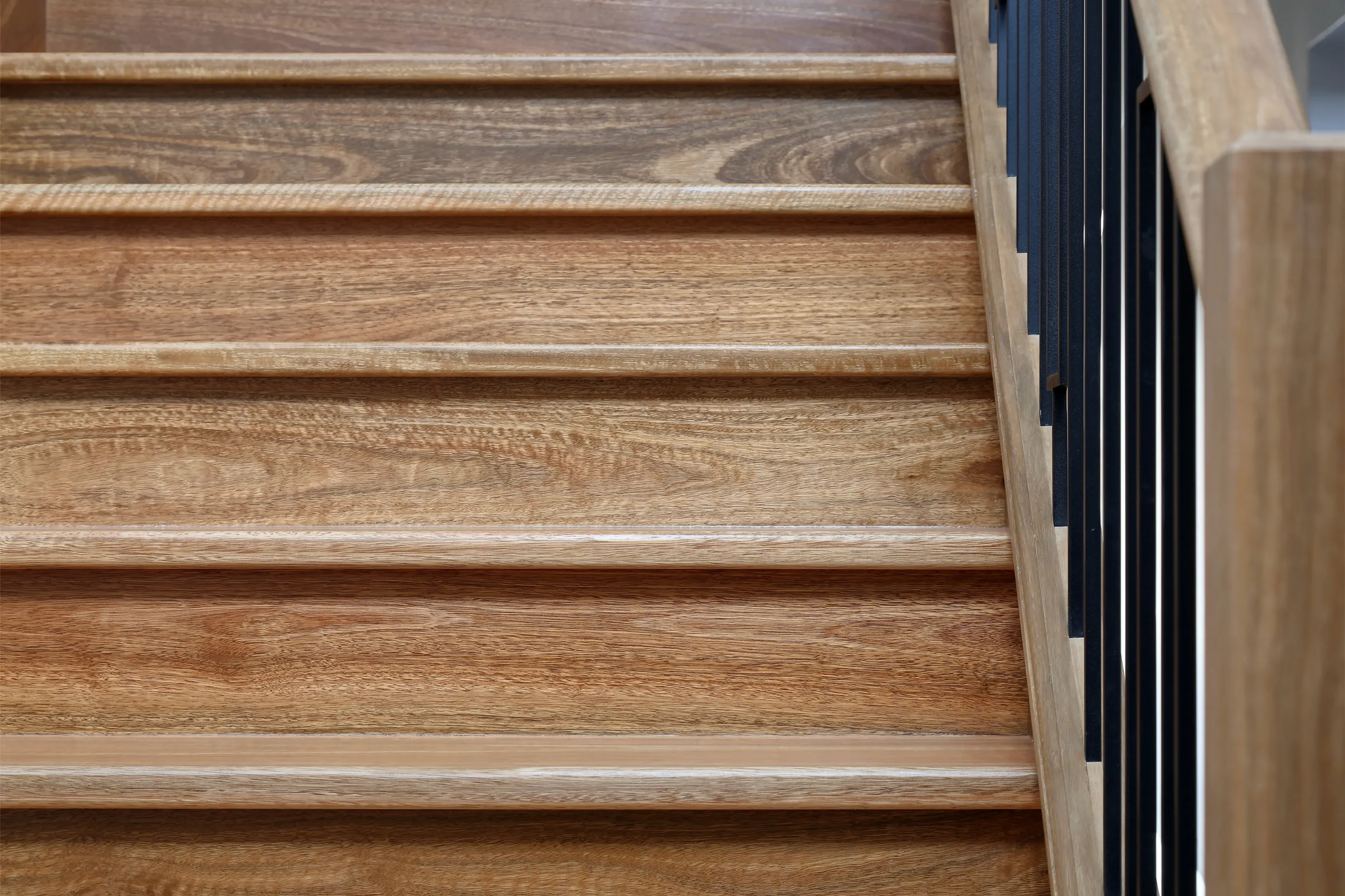 Close-up of the solid timber staircase treads beside a black iron balustrade and timber handrail