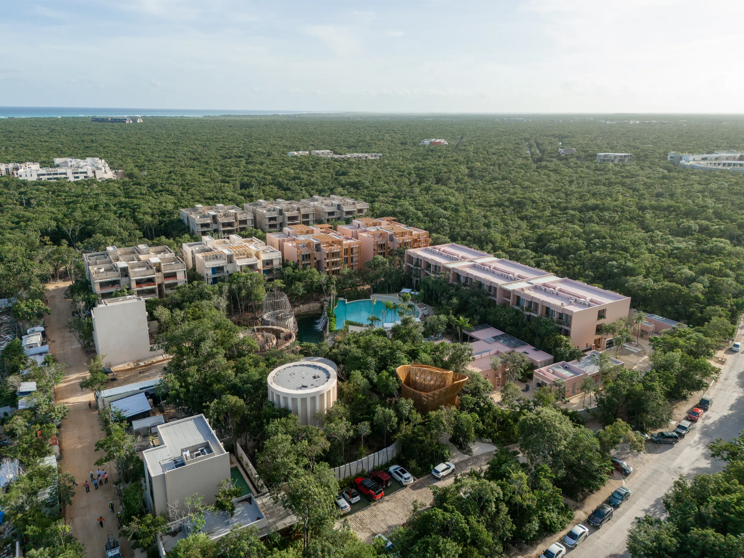 Drone shot of the Aflora residential development in Aldea Zamá, highlighting the bamboo reception tower as a central architectural landmark amidst the lush tropical vegetation.