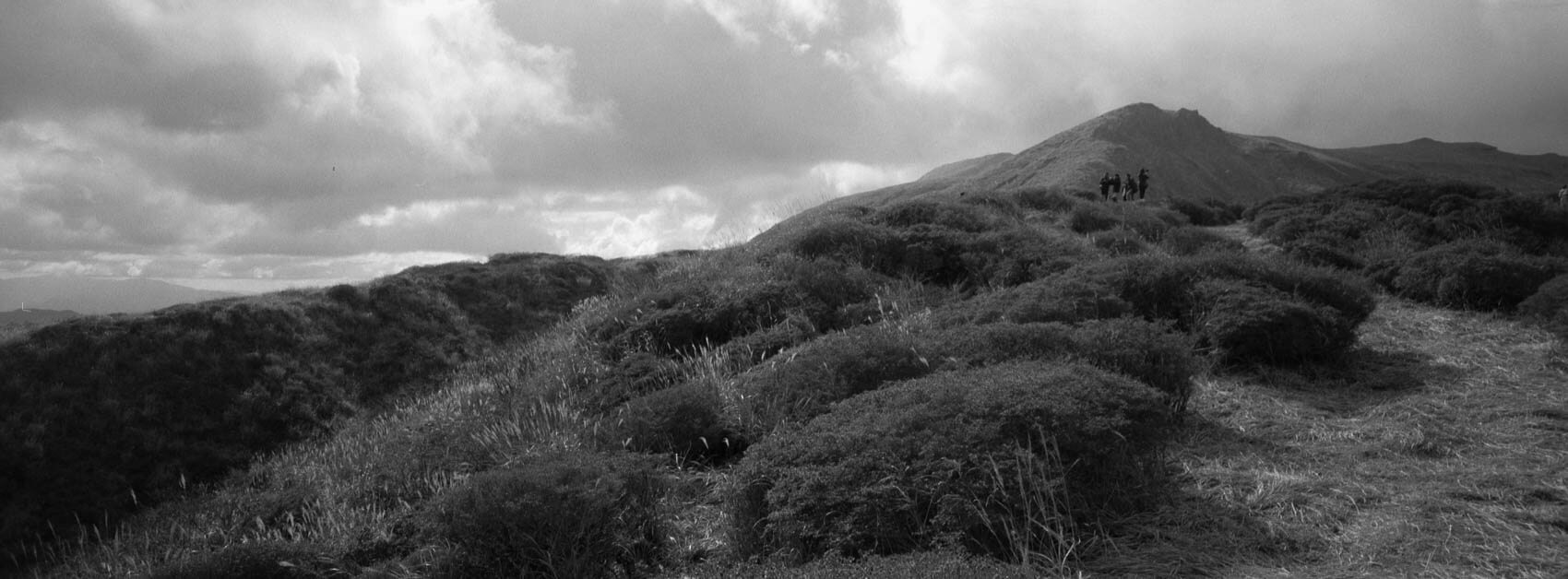 Japan hiking at Mount Aso: Lower terrain where vegetation is still fully present, black-and-white landscape with people in the back, captured on the Hasselblad XPan on film in Kyushu's otherworldly terrain.