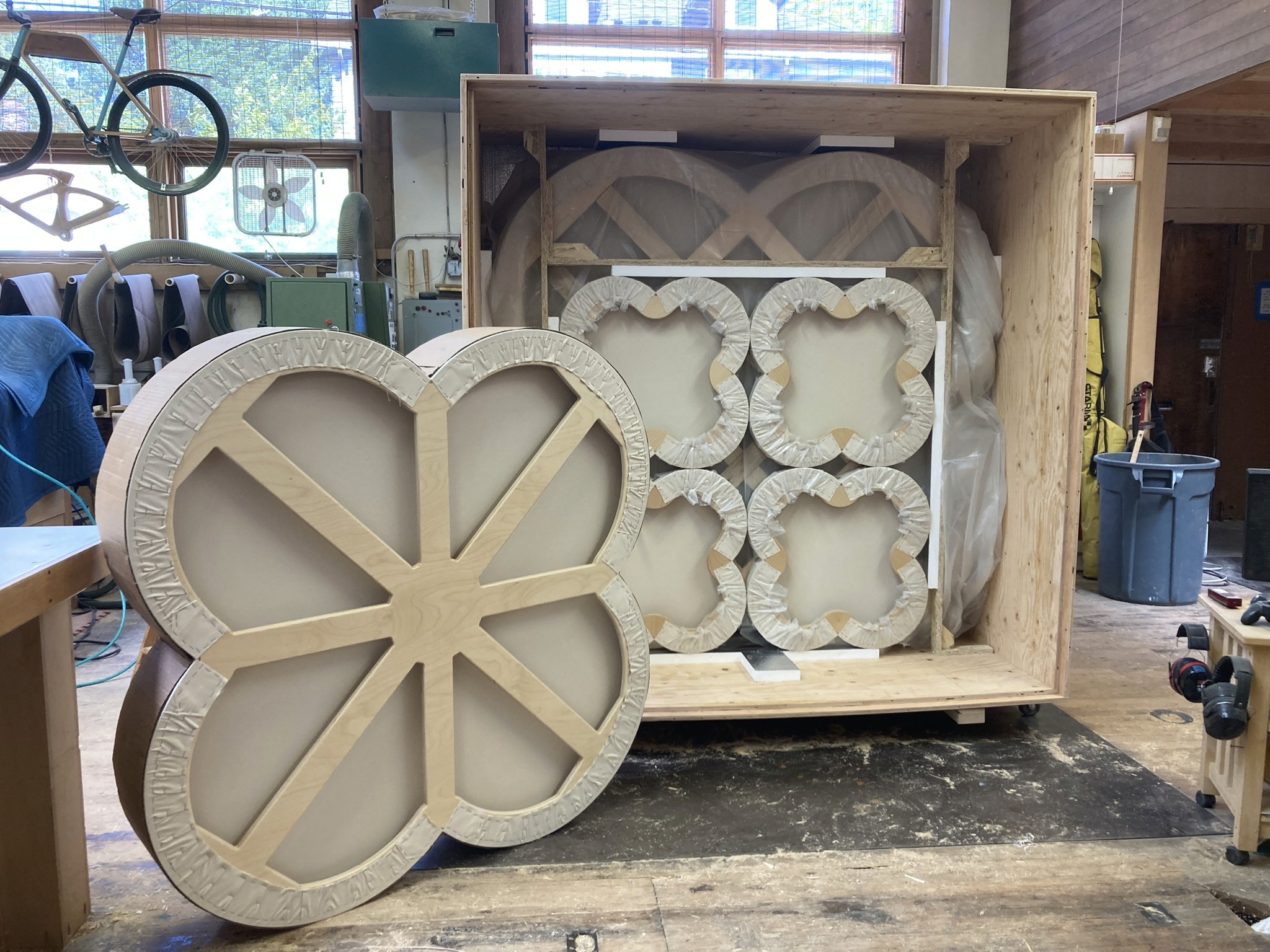 A large shipping crate is open to reveal the back of packed quatrefoil-shaped canvas stretchers for fine art painting.