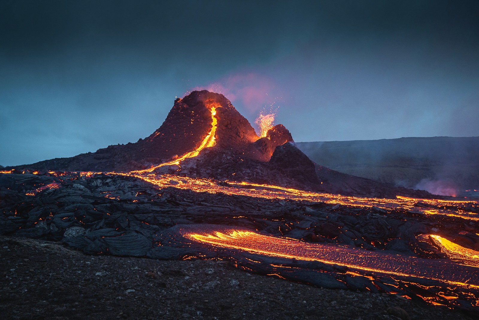 Photo by Garðar Ólafs of the 2021 volcanic eruption at Geldingadalir, Iceland, showing glowing lava flows streaming from the crater and illuminating the surrounding dark landscape.