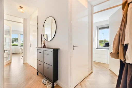 De hal van het appartement met een zwarte ladekast en een ronde spiegel.