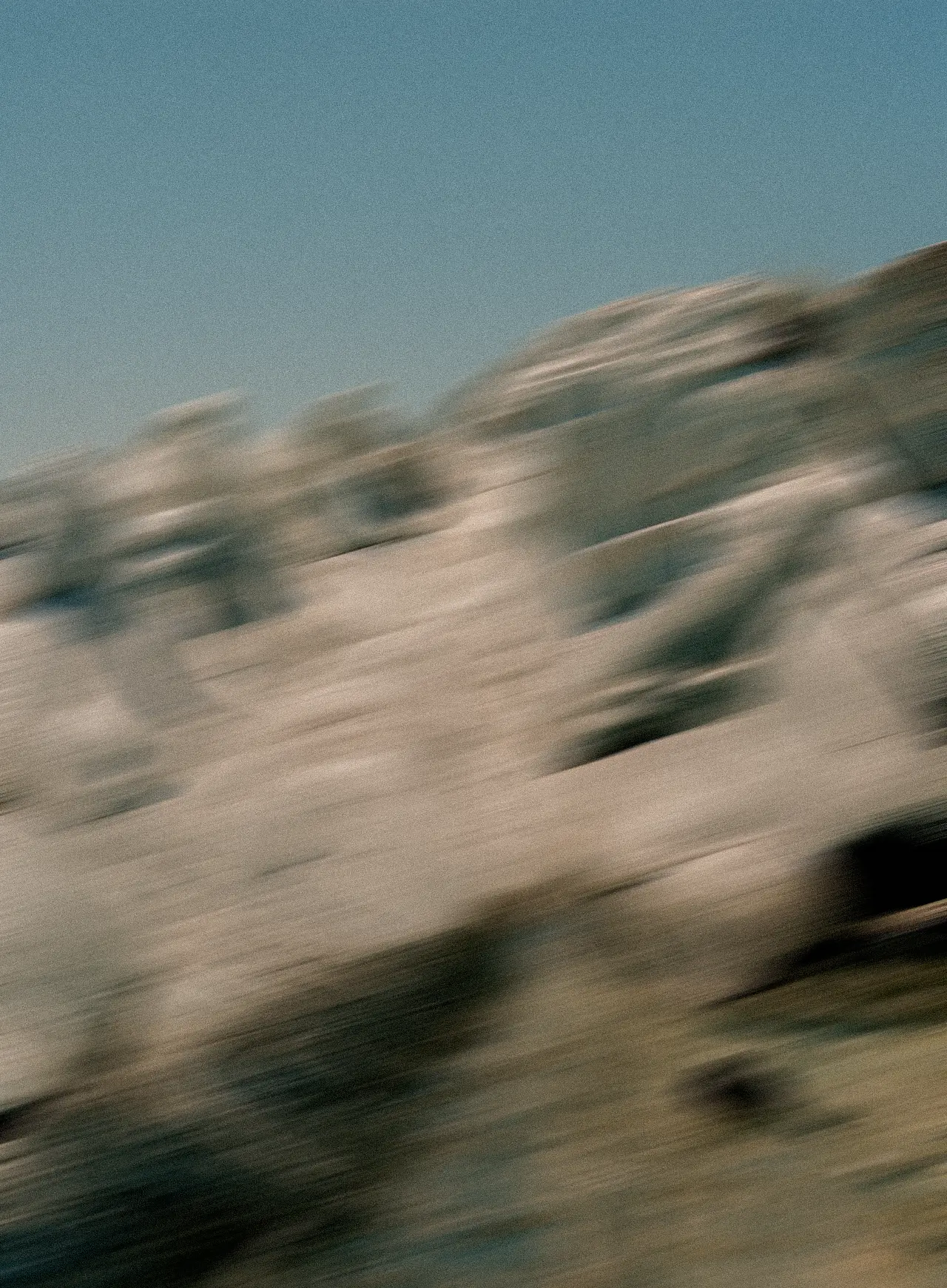 Motion-blurred landscape photo of rolling hills under a cloudy blue sky, with warm earthy tones in the terrain conveying a sense of movement.