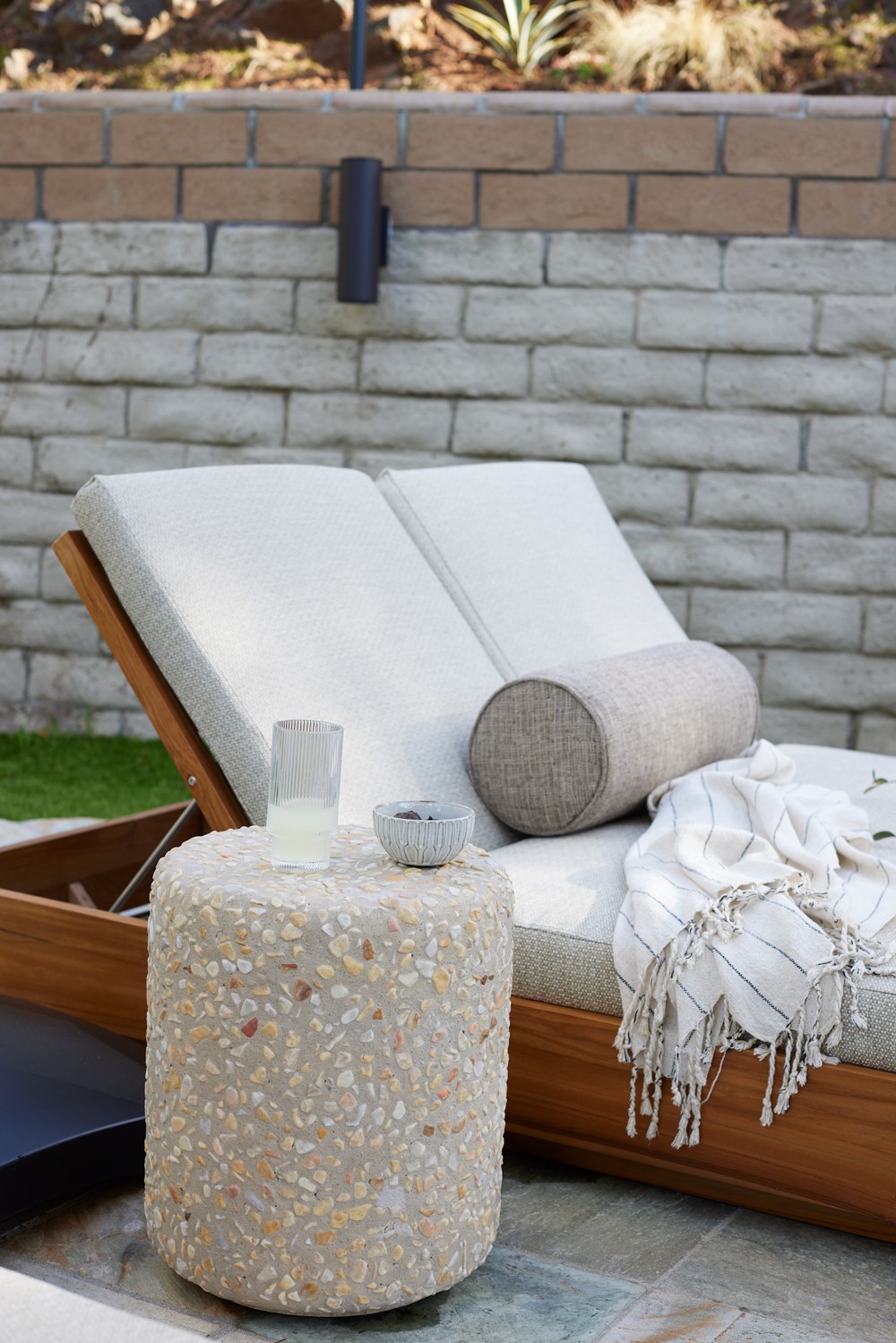 This outdoor space features a stone side table, linen accents, and a sun bed with natural wood tones