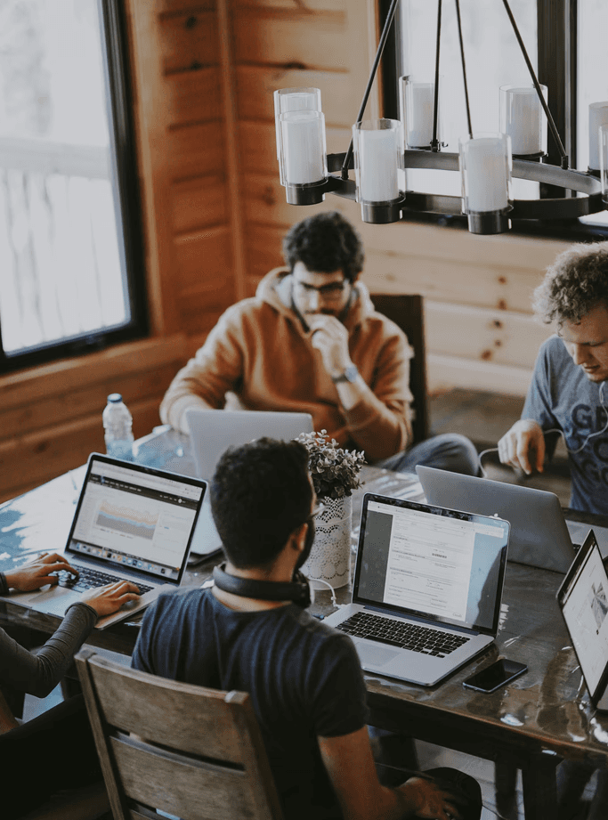 Image of a group of people working together in a collaborative setting, each focused on their laptops, suggesting a co-working environment, team brainstorming, or a project meeting.
