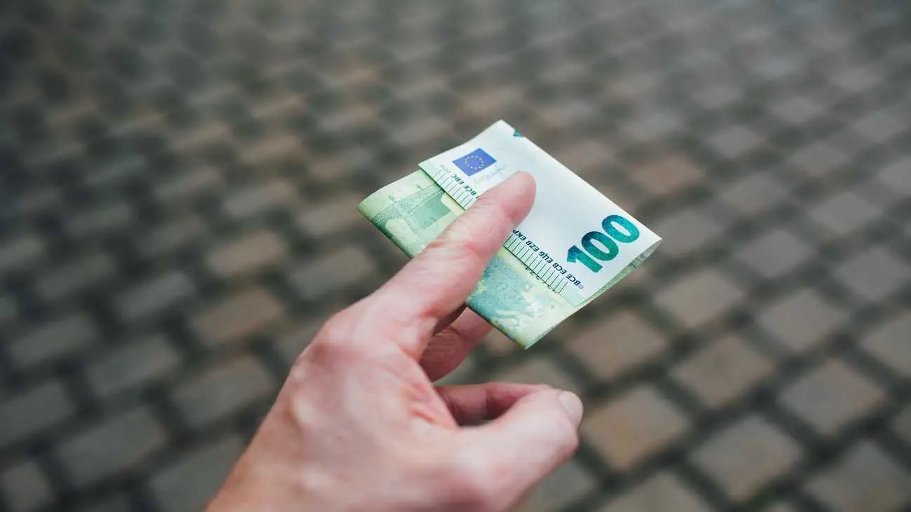 Hand holding a folded 100-euro note on paving stones – symbolising sponsorship as a source of funding for clubs and tournaments.