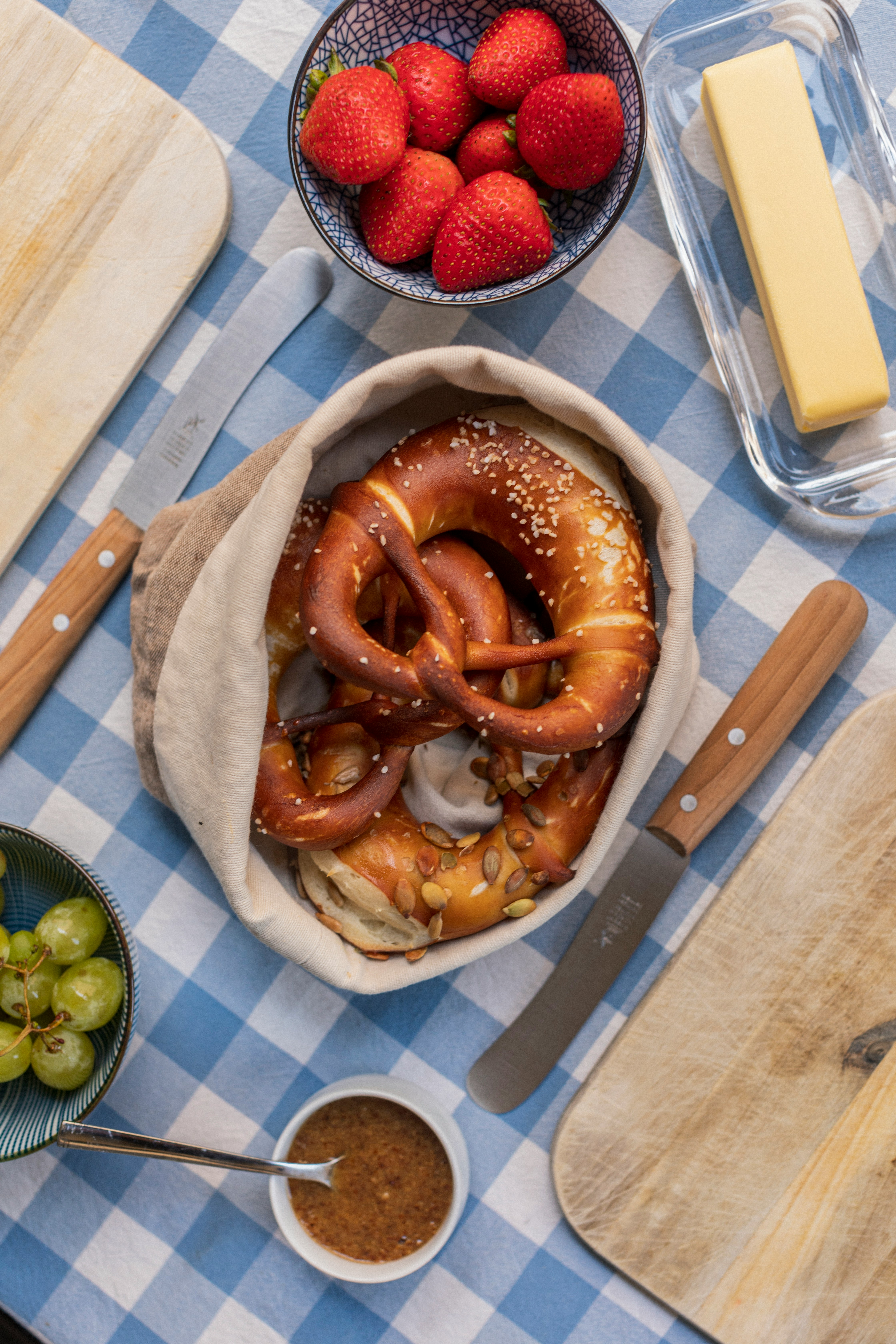 Basket of salted pretzels on a checkered tablecloth with knives nearby
