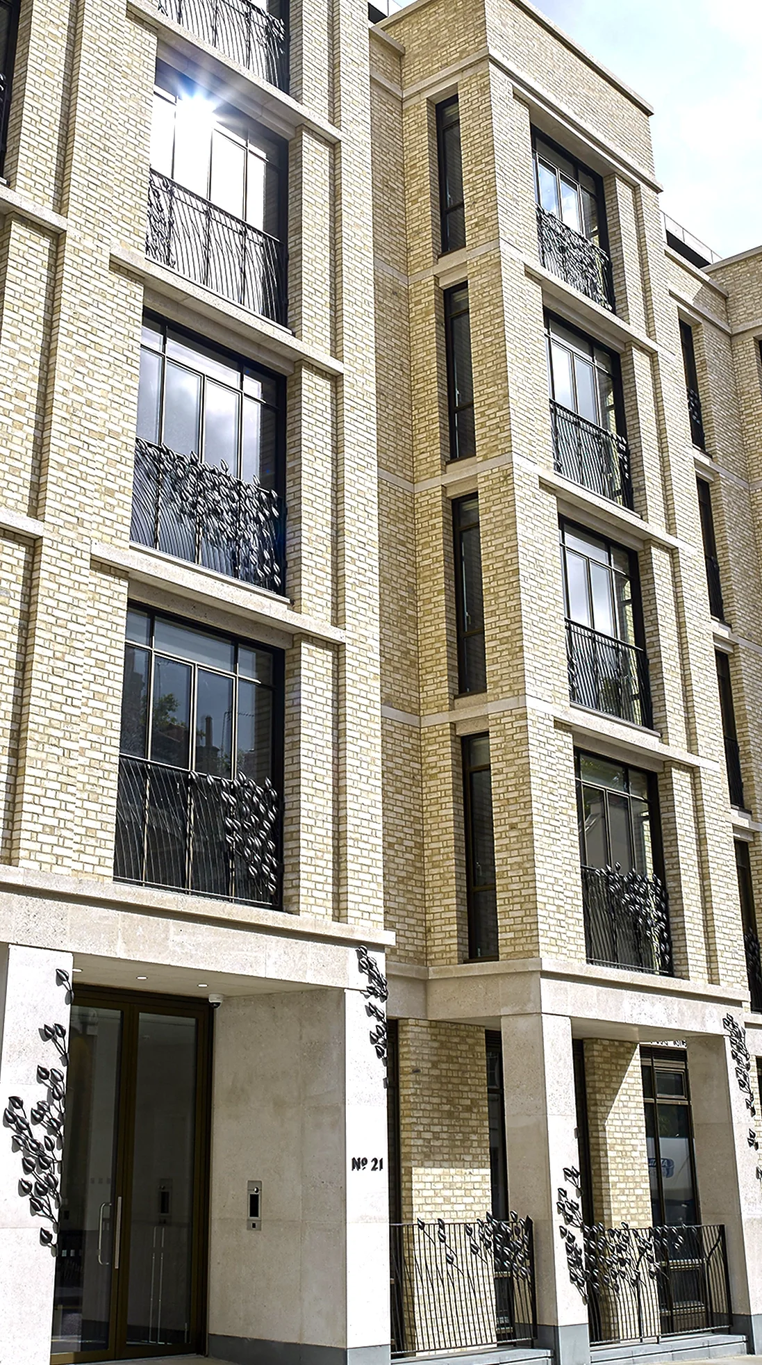 The exterior facade of a luxury cream-brick residential building featuring bespoke bronze balconies and leaf-motif decorative gates. An expansive architectural objet d’art project created by Shaun Leane's independent studio.