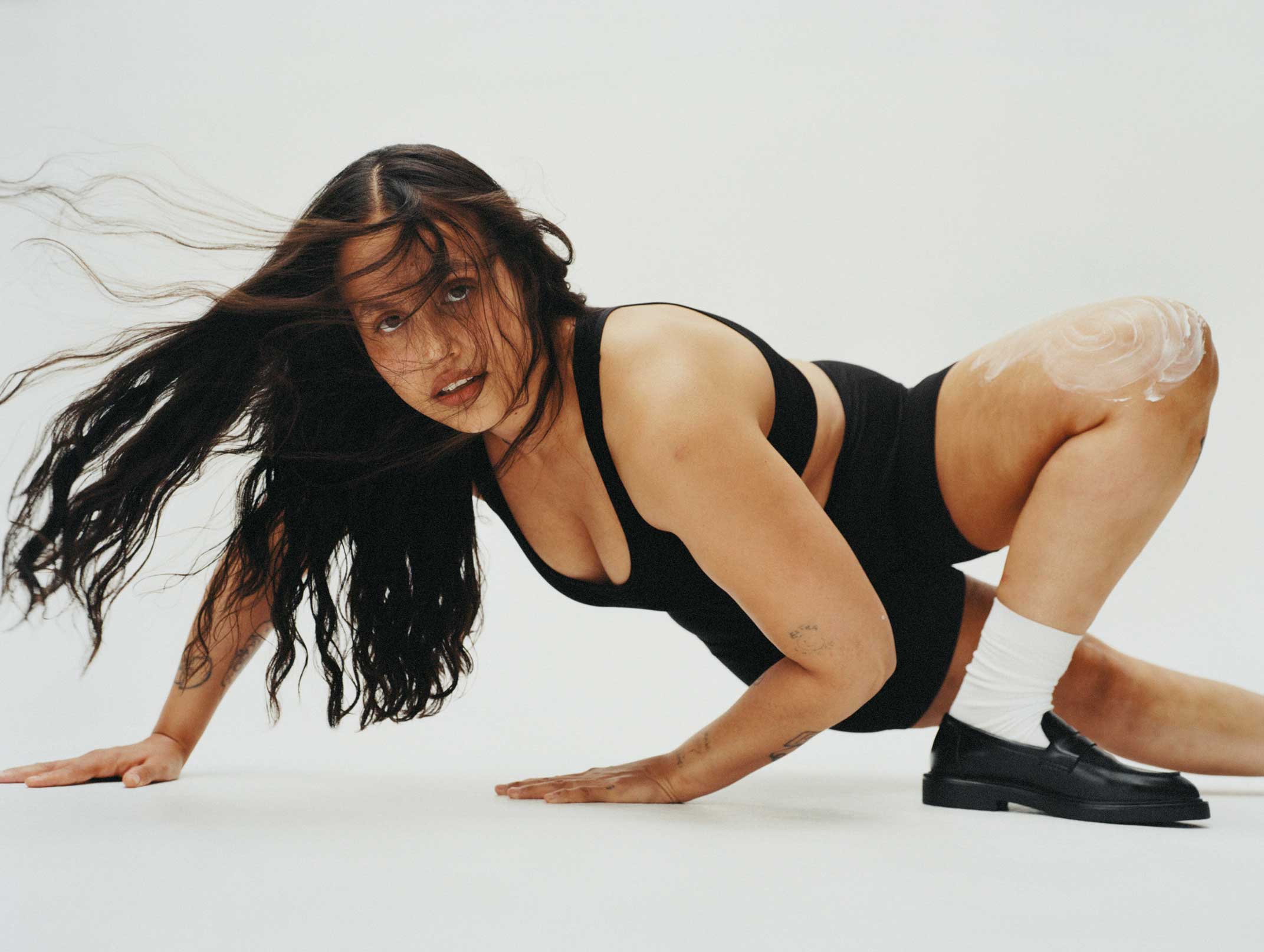 Woman in black sportswear and white socks with black loafers posing low to the ground.