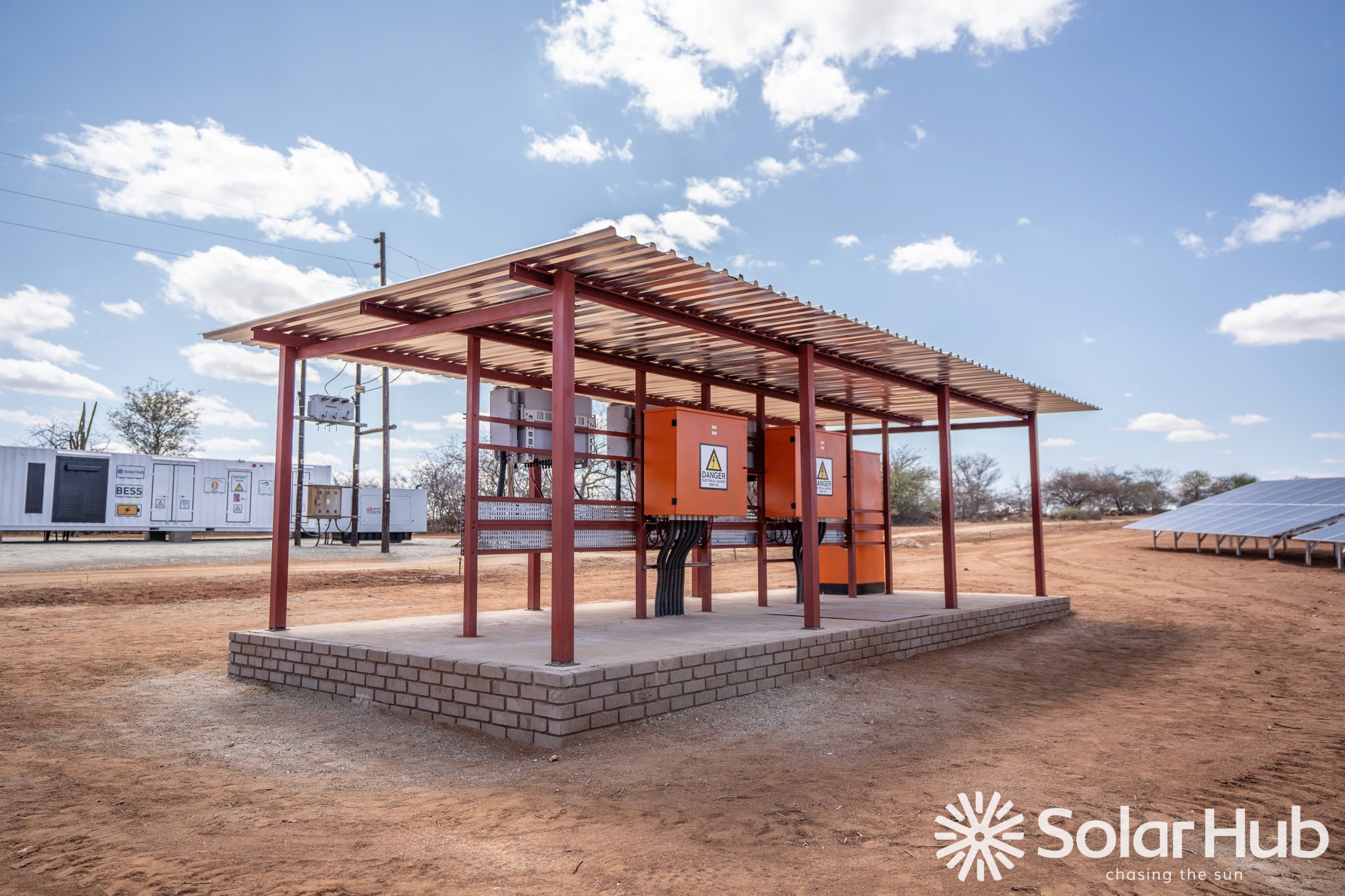 Woman in a beige blazer handing a document to someone, standing near a window with a city view. She looks professional and confident.