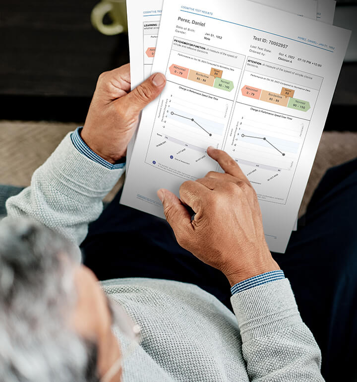 Overhead view of someone reviewing cognitive assessment documents, holding papers and a smartphone displaying memory test results beside a laptop.