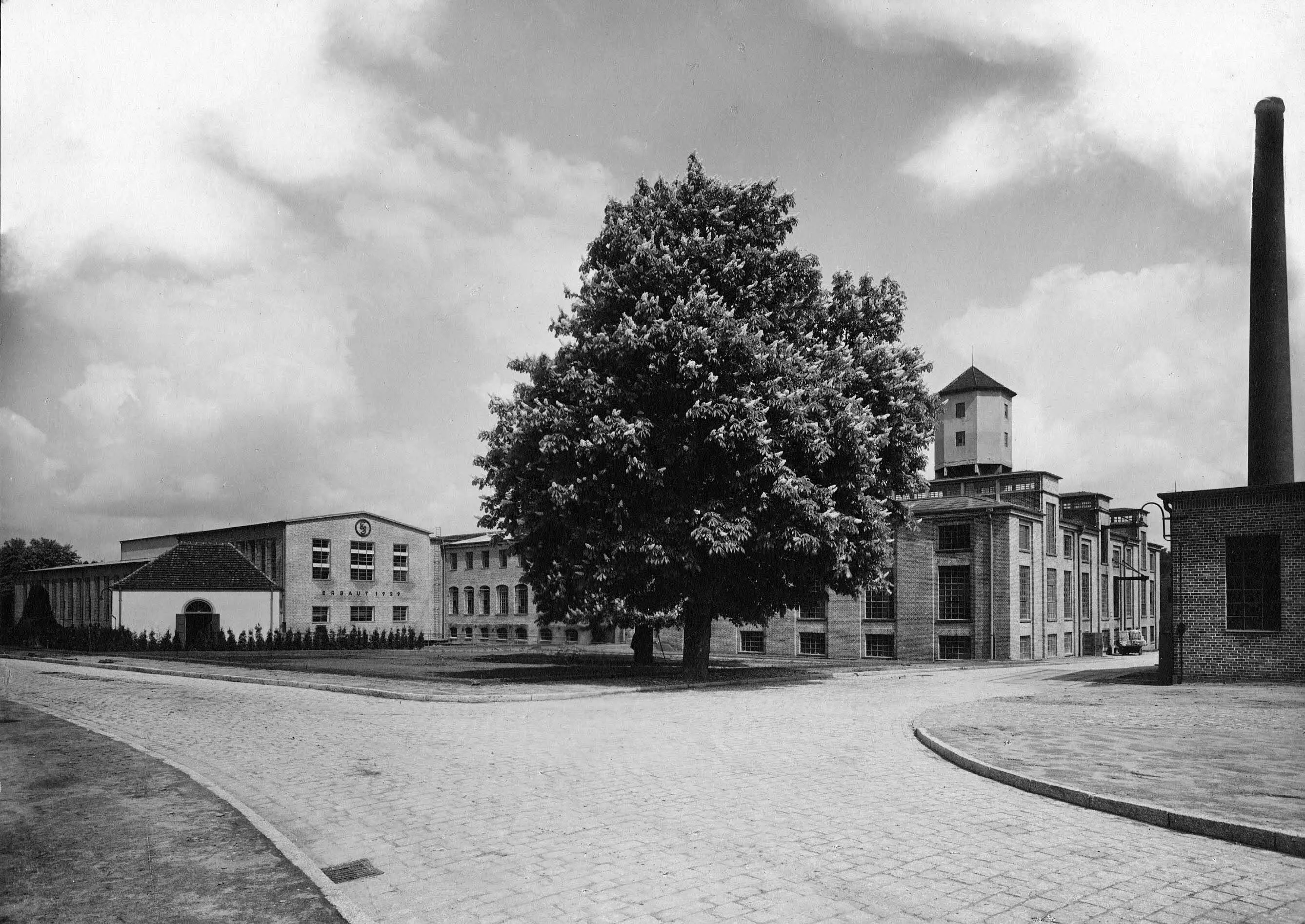 Historisches Foto (1929-1938) vom Tor auf das Pförtnerhaus, die Hertleinhalle, das Hallenensemble und den Wasserturm auf dem Gelände der Papierfabrik Wolfswinkel in Eberswalde