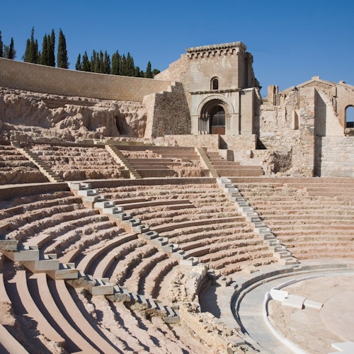 在晴朗的蓝天下，古罗马圆形剧场展现了分层座位和风化的石质建筑。