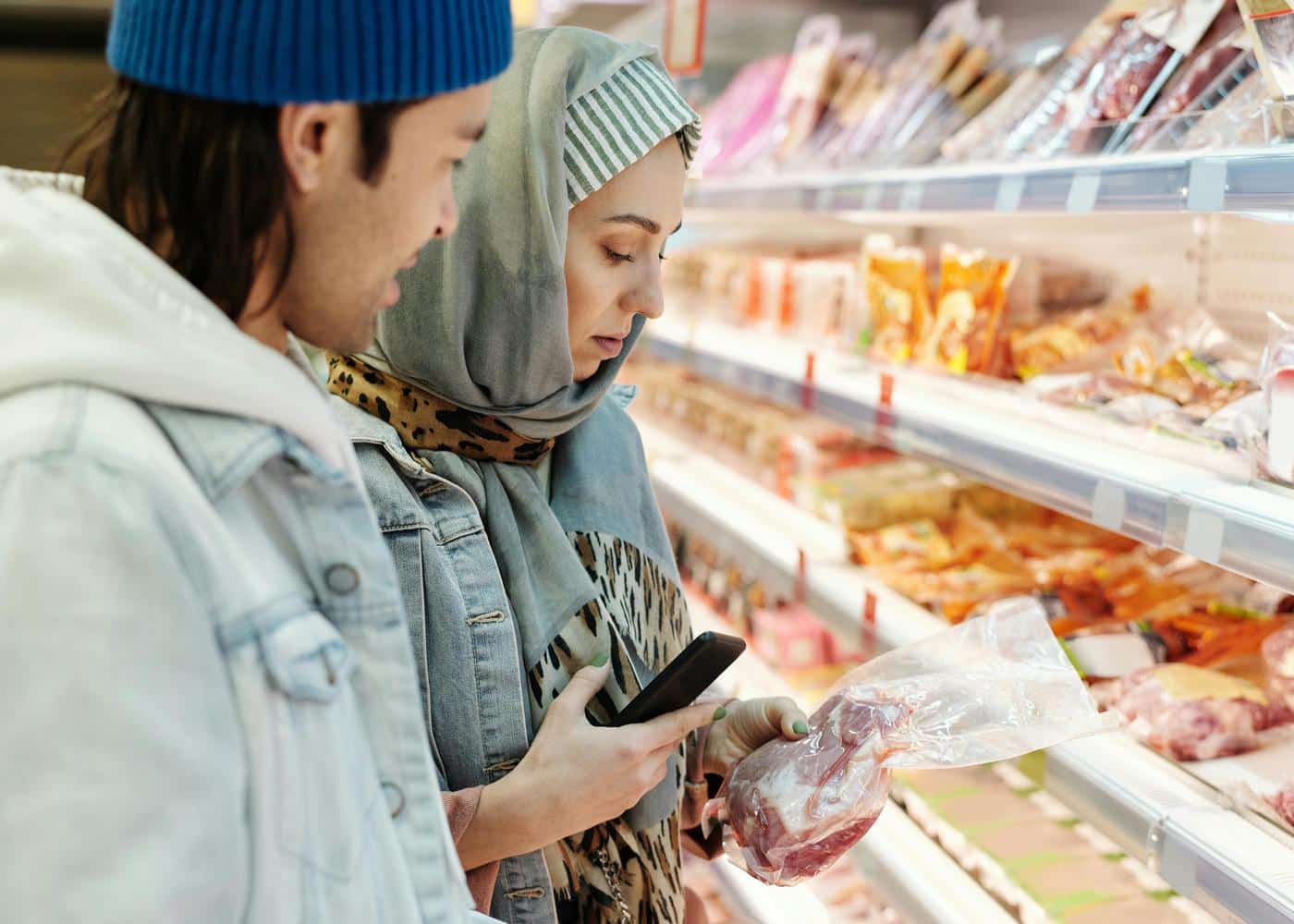 Couple buying meat at a grocery store with phone in woman's hand