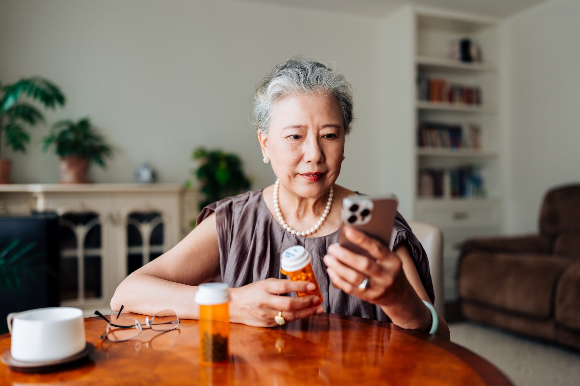 Older woman holding medication and using smartphone