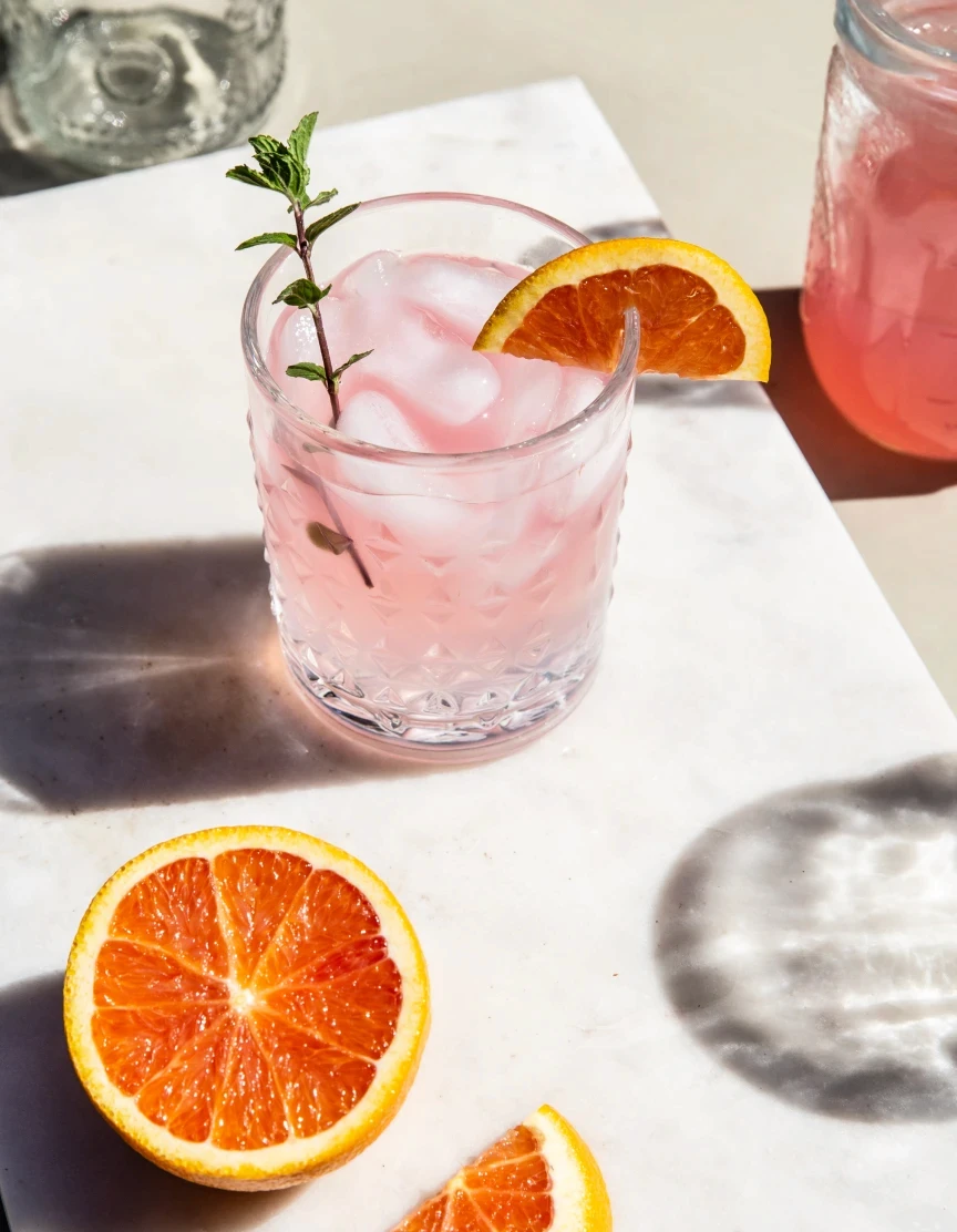 A pink cocktail and an orange in sunlight.