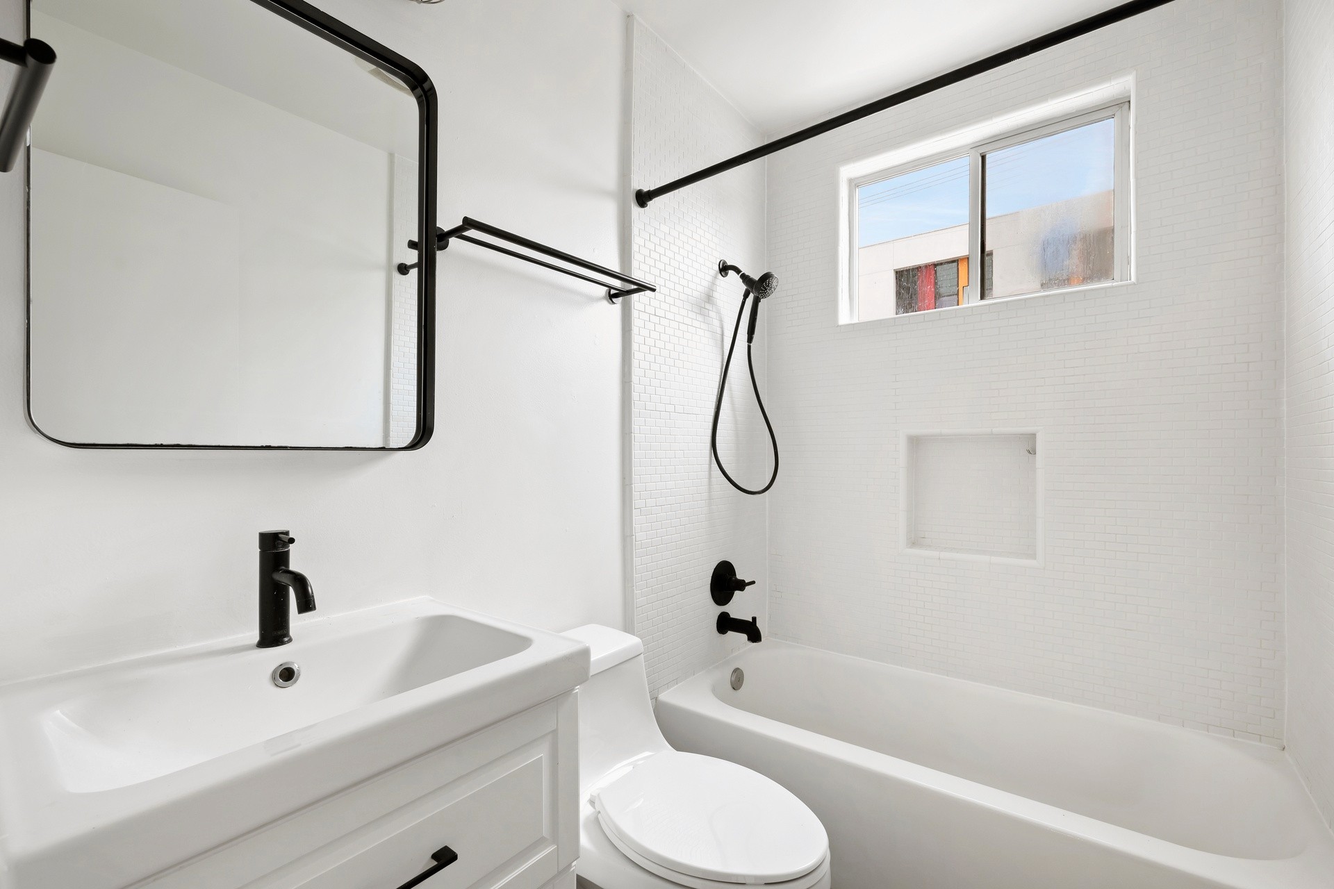200 N Rampart renovated bathroom with white tile walls, updated vanity, black fixtures and bright light.