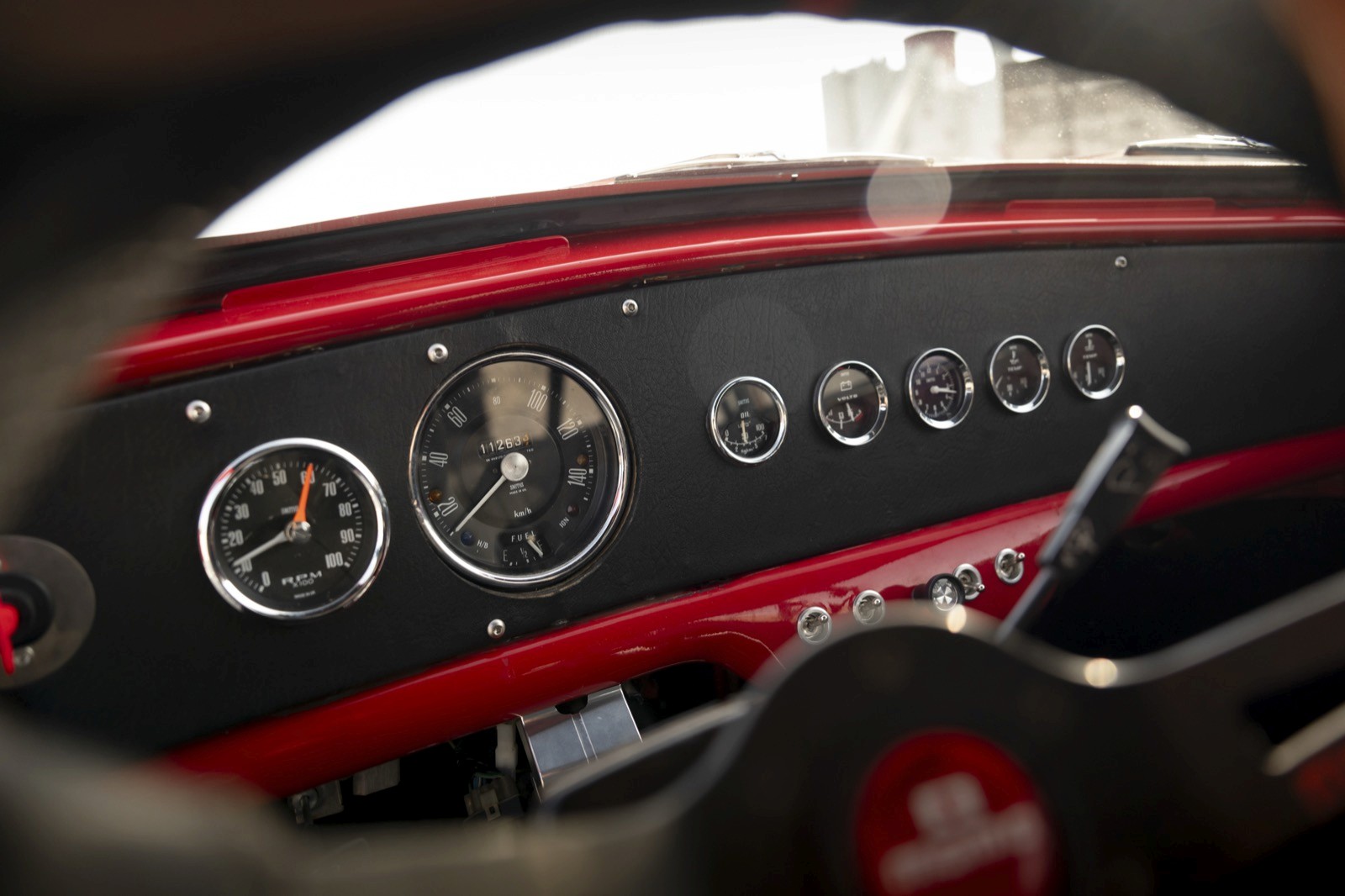 Close-up of a vintage car dashboard with gauges and a steering wheel, featuring a classic red and black design.