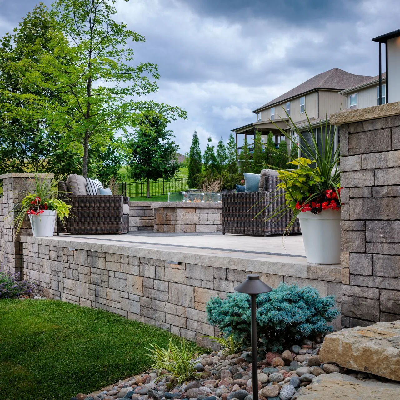 A terrace above the lawn A raised garden terrace with lounge chairs and a low fire feature sits above a textured wall, lawn and planted borders.