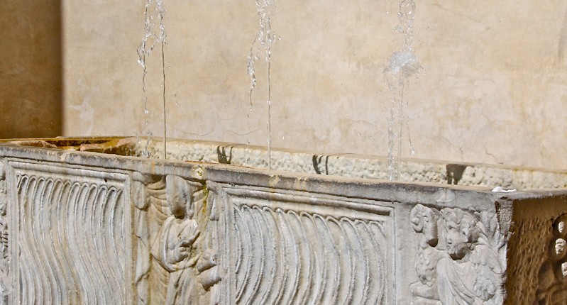 A photo of an old stone fountain spring with engravings on the side.