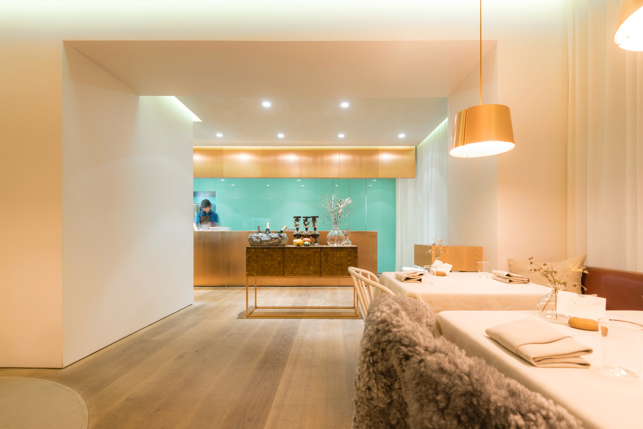 A modern hotel lobby with a reception desk, a dining area with white tables and chairs, and a pendant light.