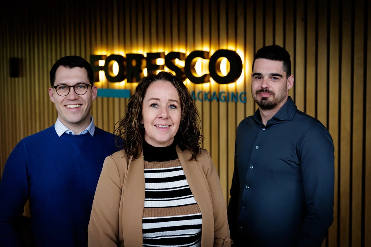 Three Foresco colleagues in front of the illuminated company sign