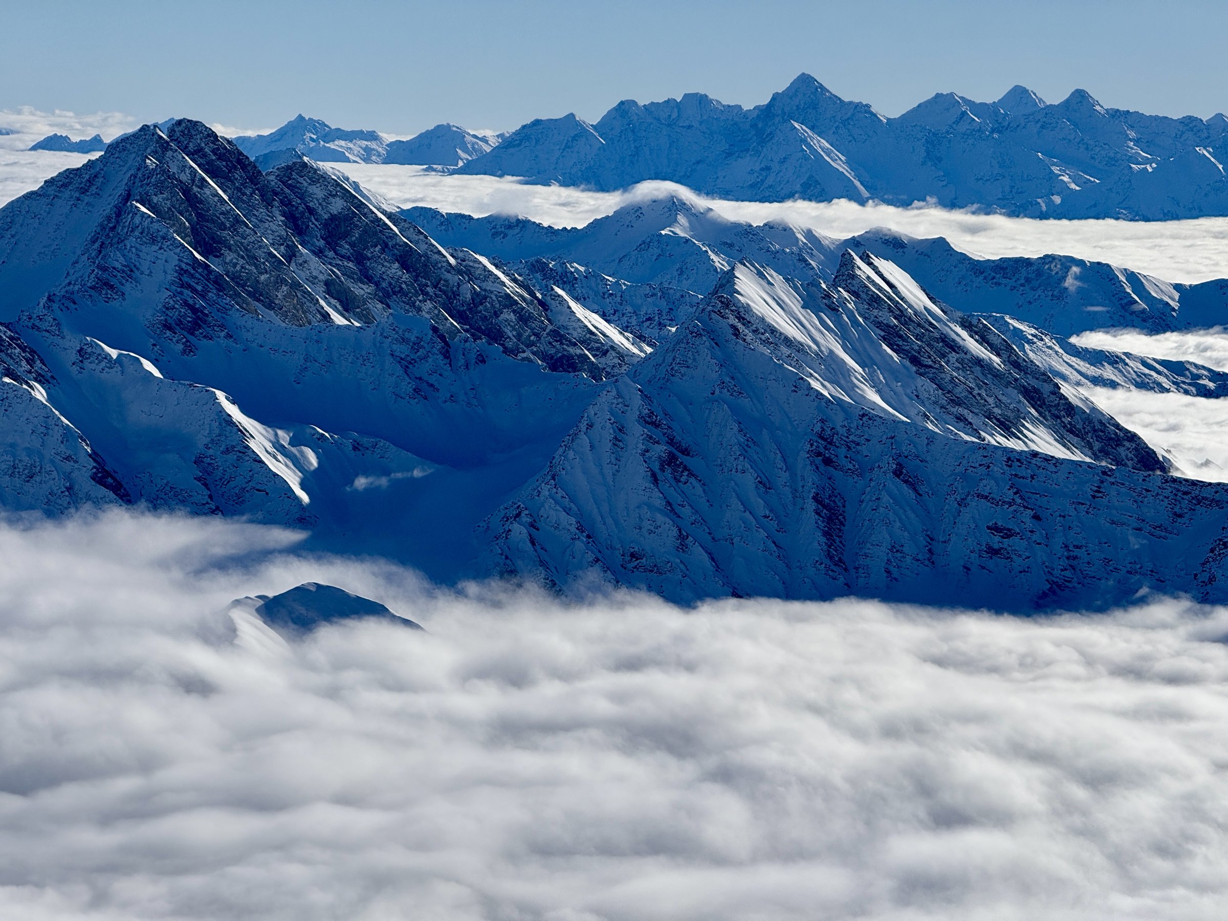Telephoto view over a sea of clouds with receding snow-covered Alpine ridgelines near Mont Blanc, Italy