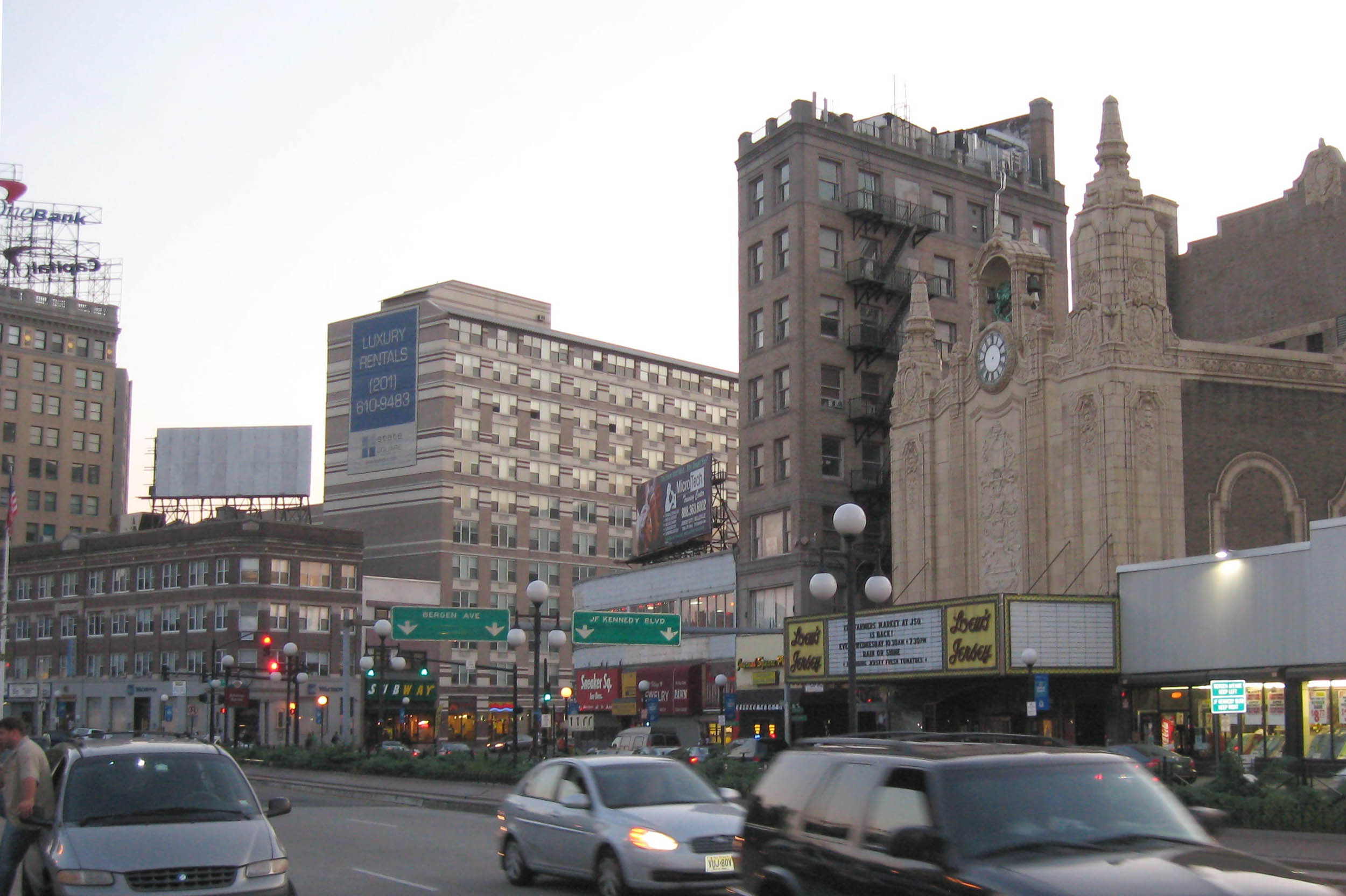 Cityscape featuring buildings and parked cars in an urban setting during twilight.