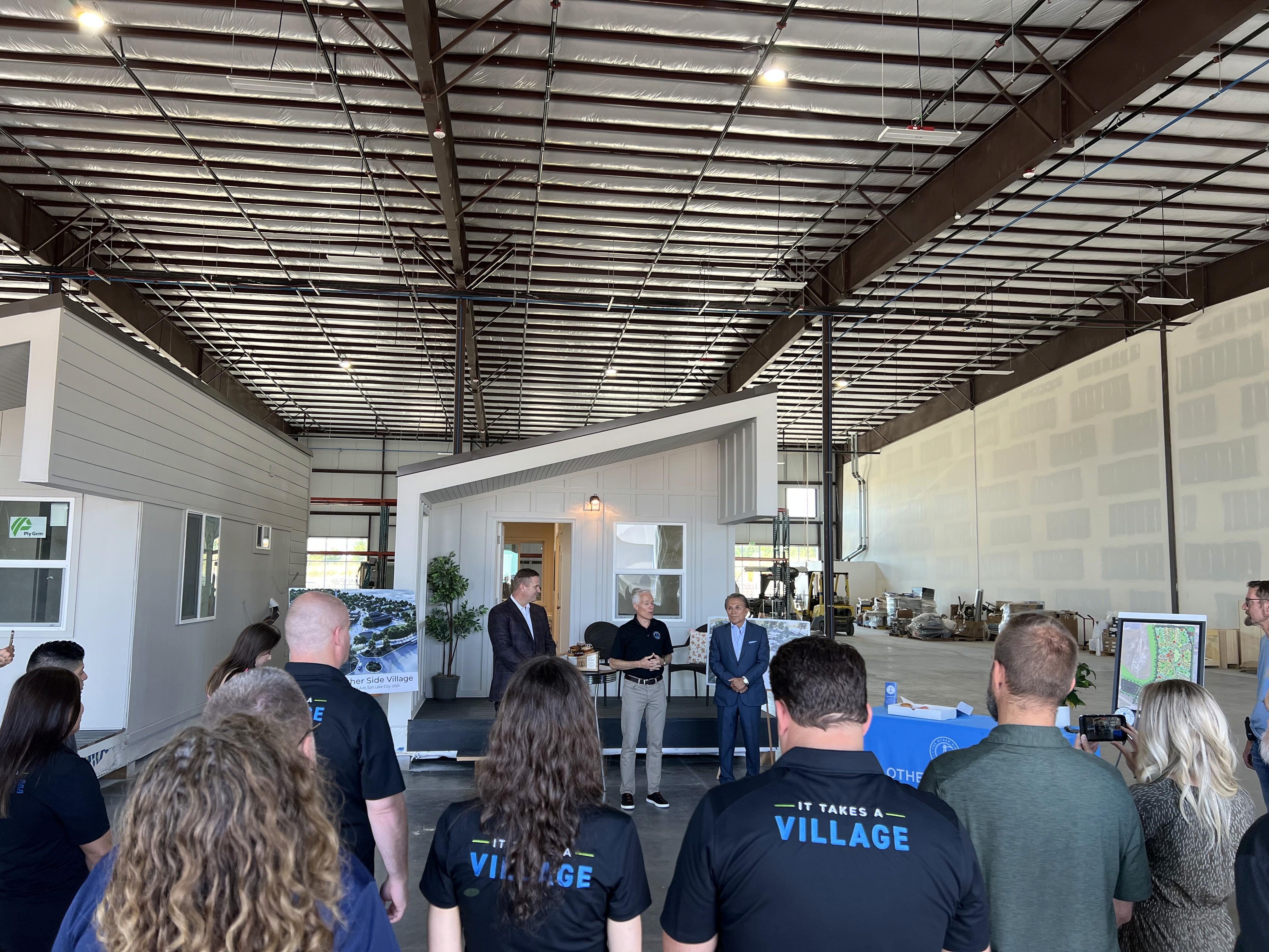 A group of people in our manufacturing facility speaking in front of a modular home.