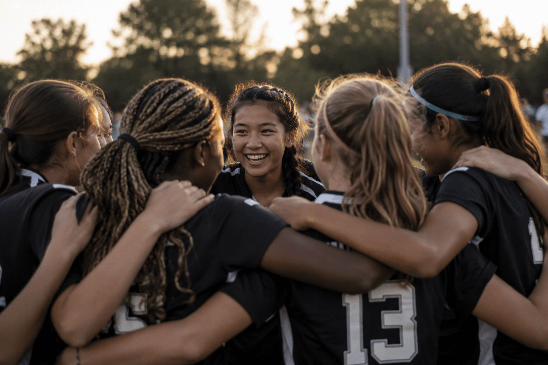 Youth soccer players in a team huddle during an outdoor practice at sunset.